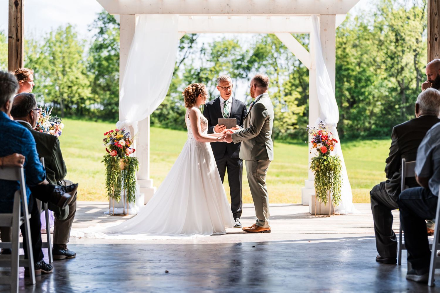 Bride and groom exchange vows at an outdoor wedding ceremony under a white arch.
