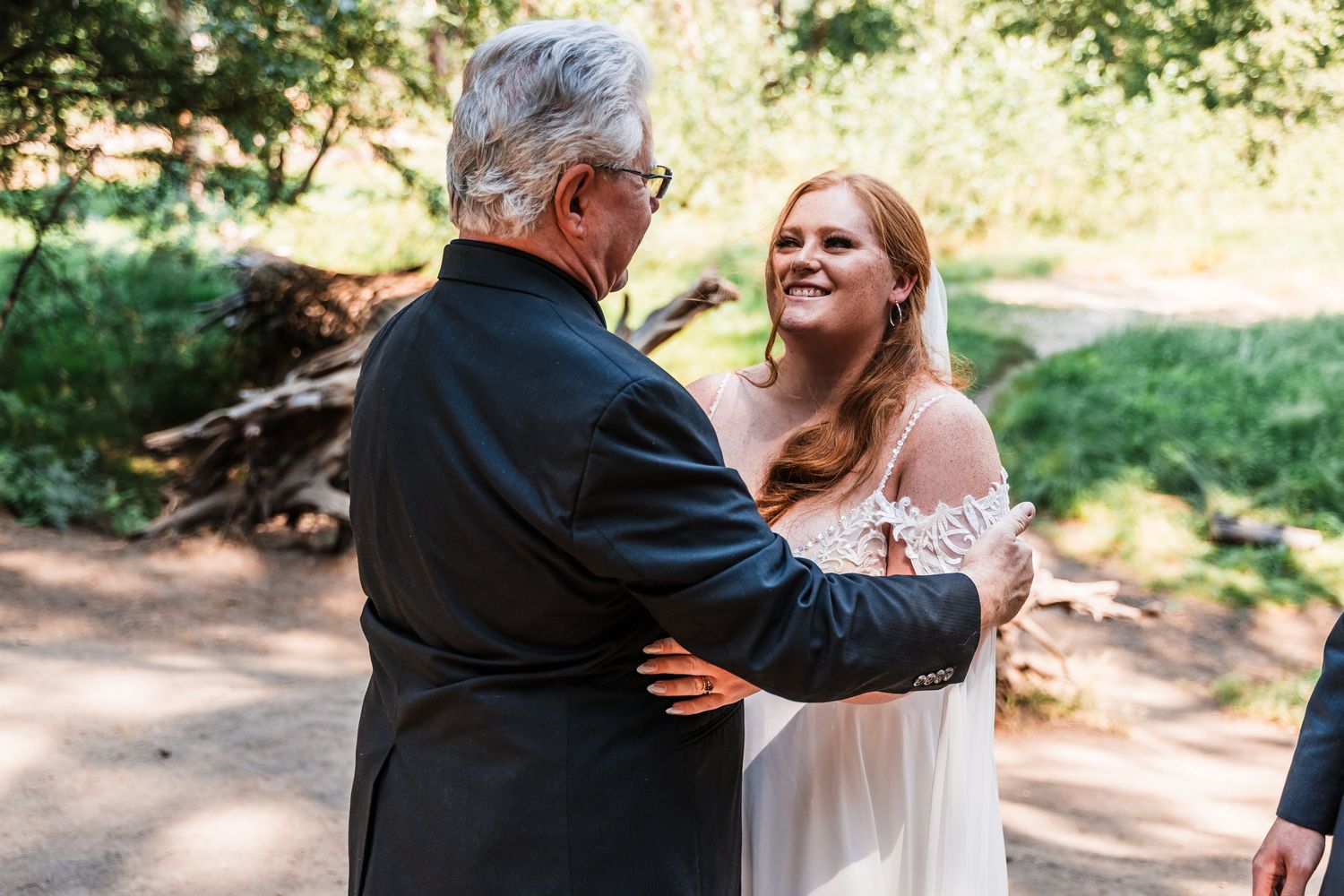A tender moment captured between a couple dancing together on a sunlit wooded path.