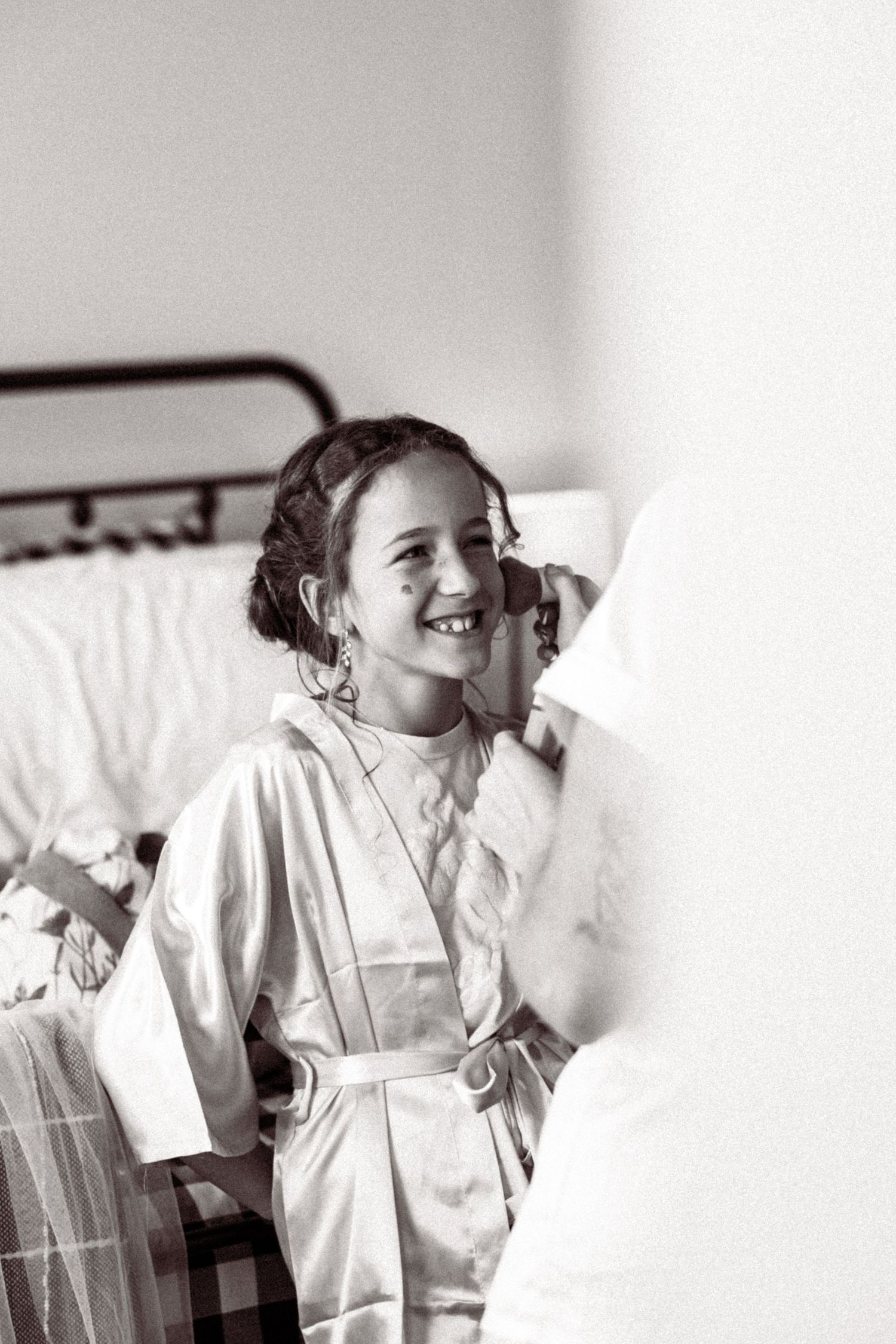 A black and white photo shows someone in a white robe getting ready during wedding preparations.
