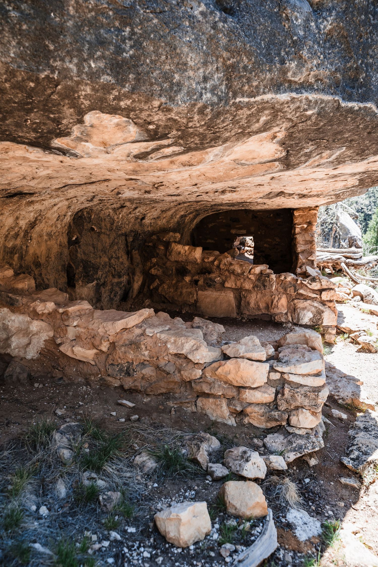 Ancient stone ruins with a cave-like entrance and stacked rock wall beneath a natural rock overhang formation.