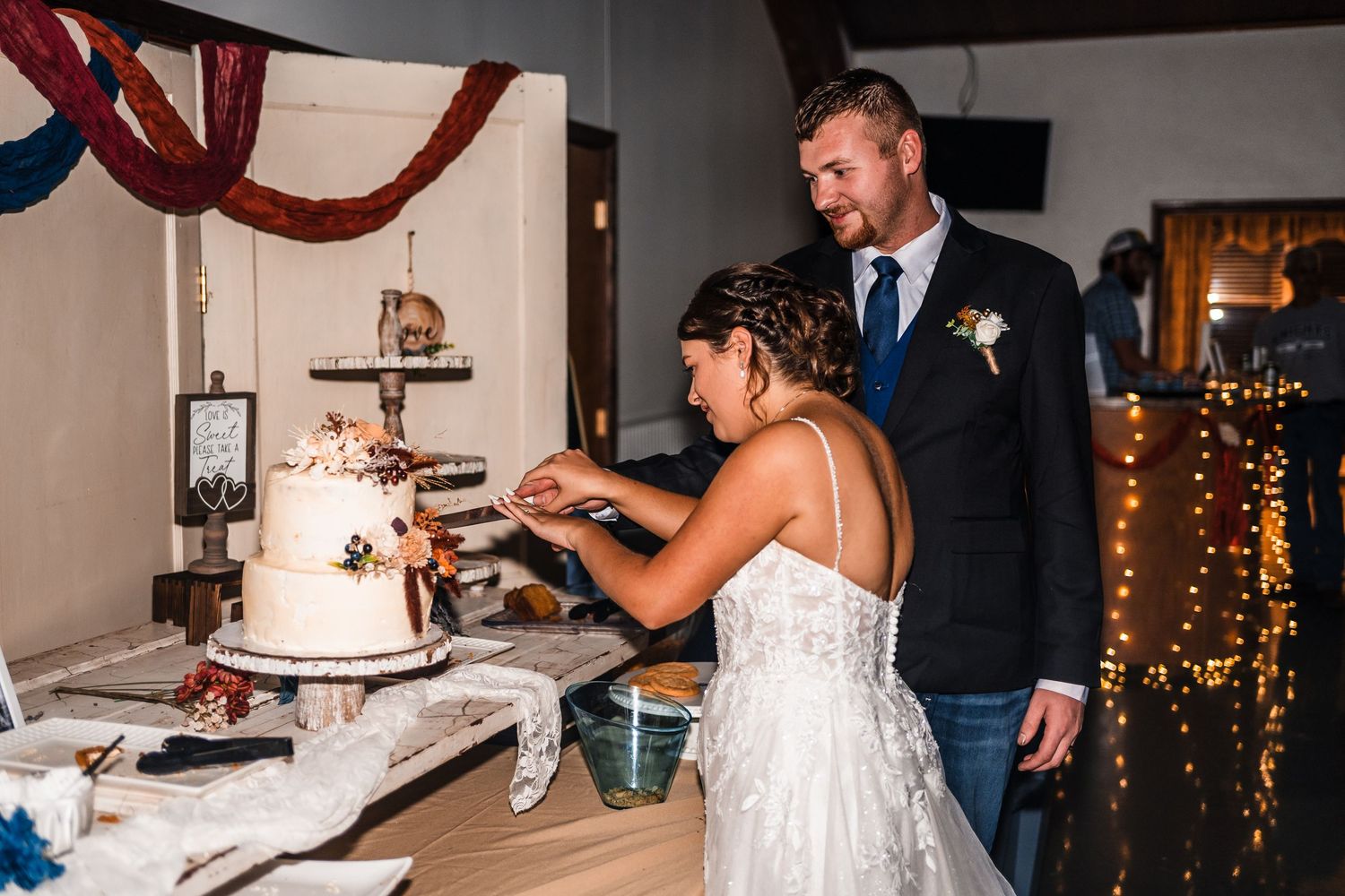 Wedding reception guests gather around a white tiered cake during the cutting ceremony.