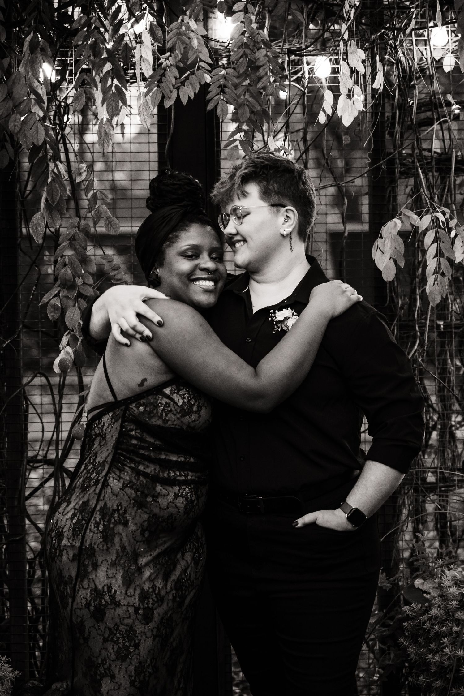 Black and white portrait of couple embracing among garden vines.
