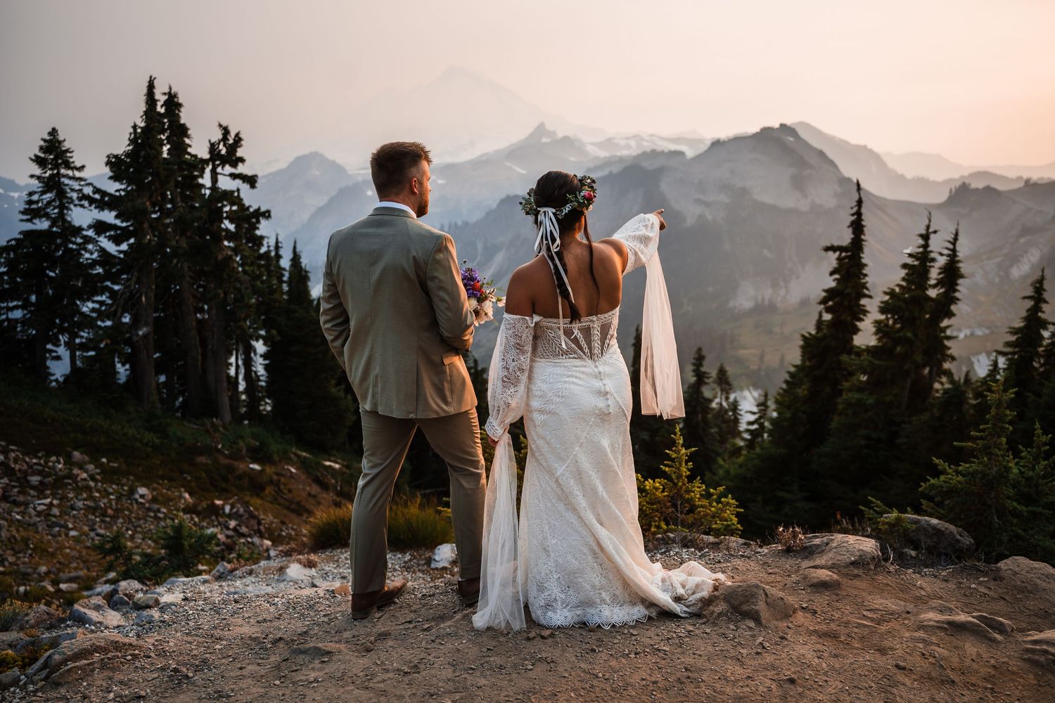 A couple in wedding attire silhouetted against a dramatic mountain landscape at sunset.