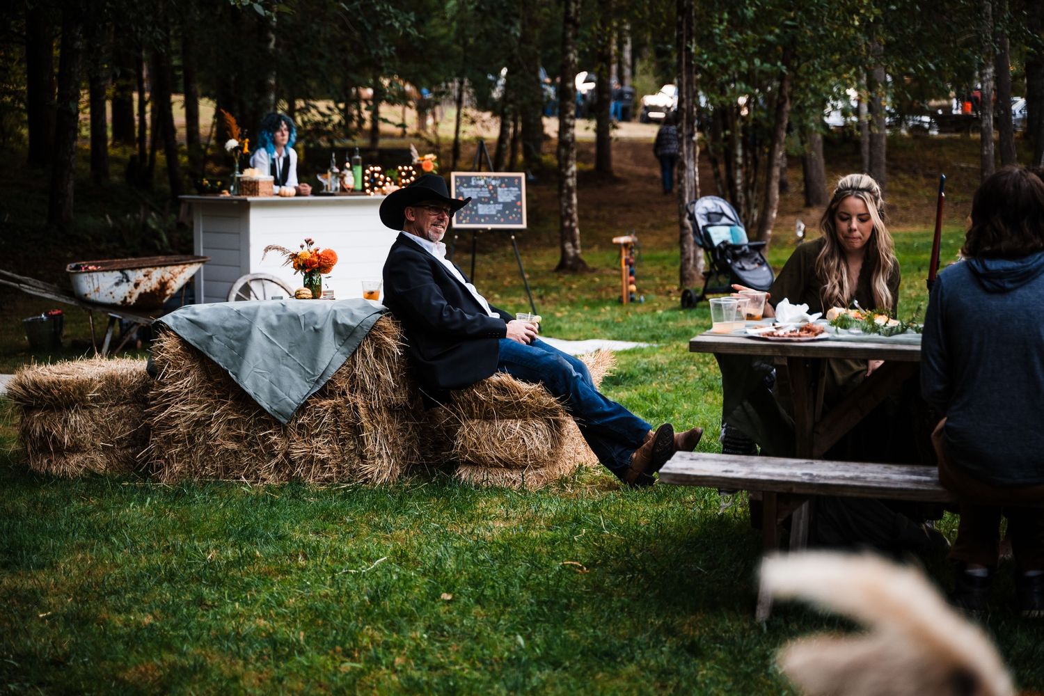 Rustic outdoor party setup with hay bale seating and decorated tables in a forest.