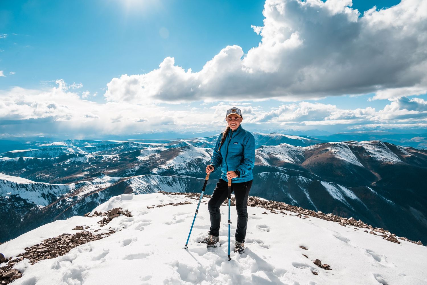 Hiker standing on snowy mountain peak with dramatic mountain landscape in background.