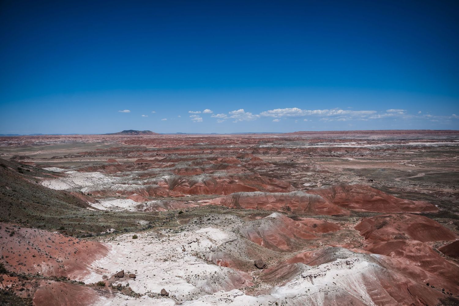 Colorful striped layers of red and white rock formations stretch across a desert landscape under bright blue skies.