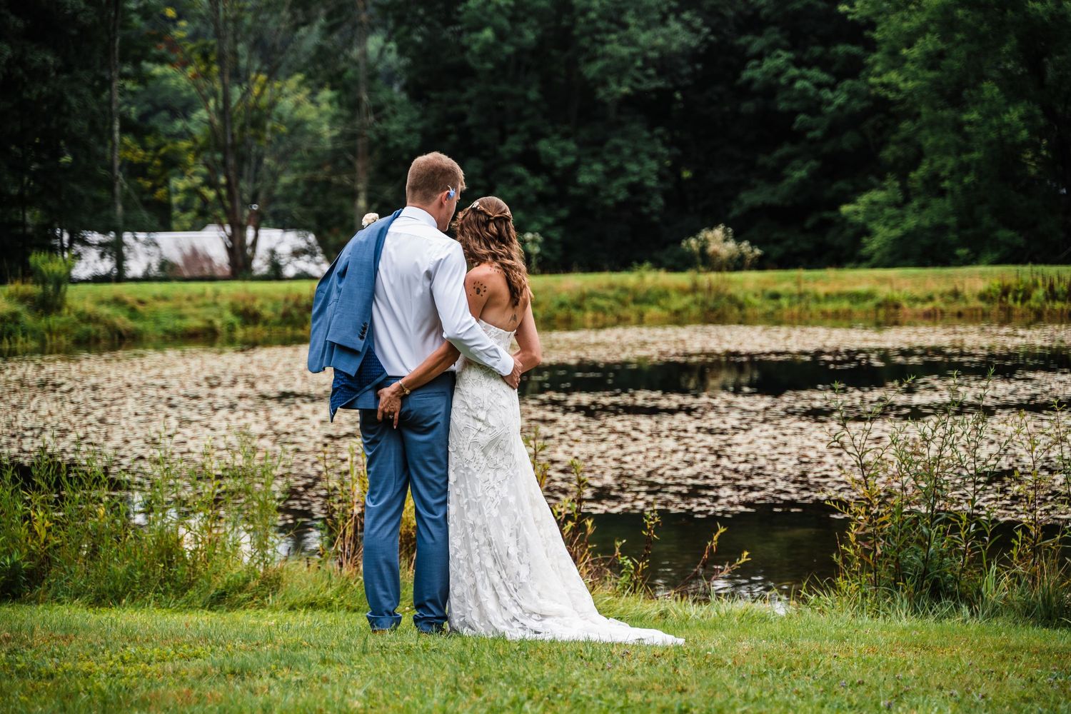 A scenic wedding photo showing a couple standing by a serene pond surrounded by lush greenery.