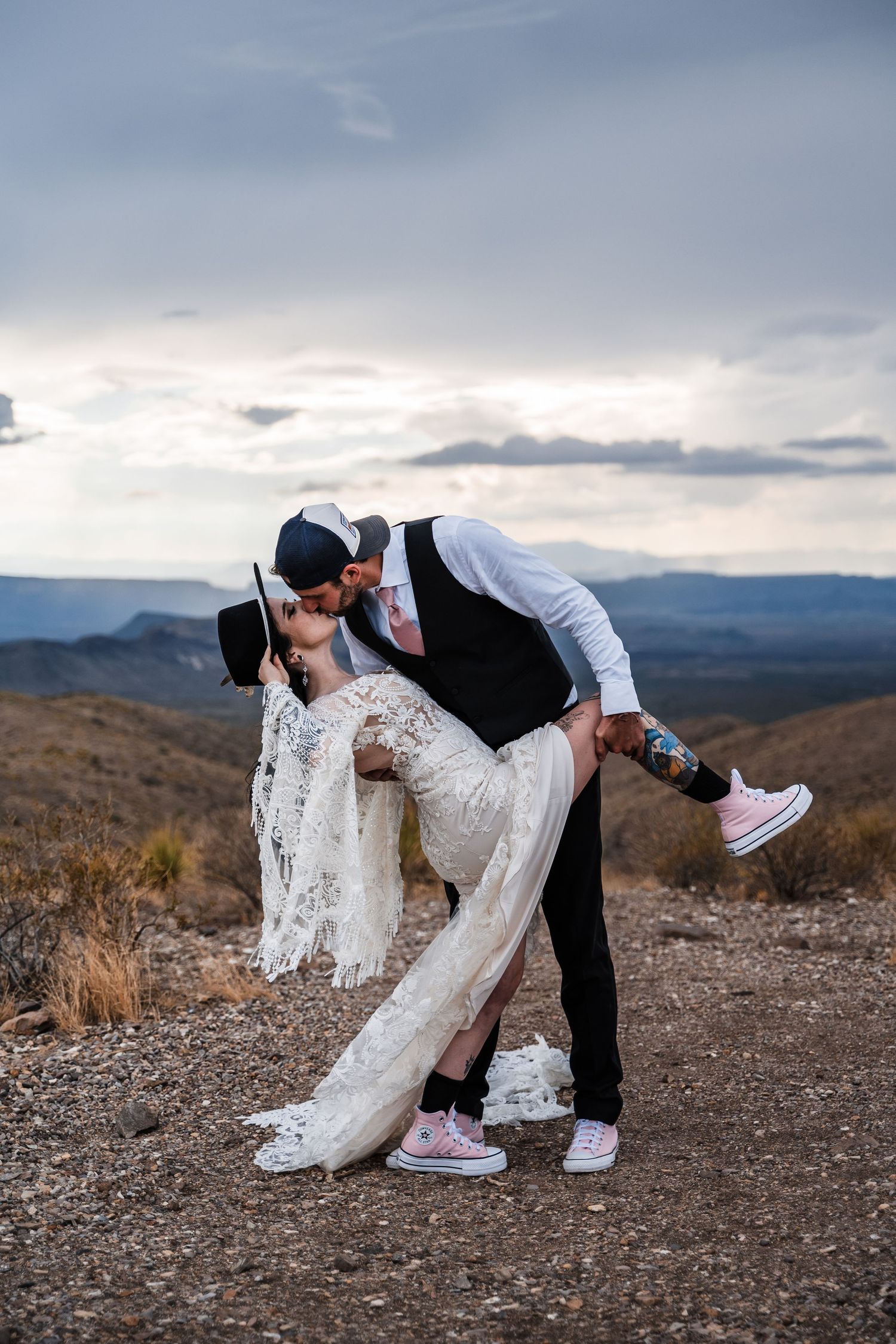 Romantic dip pose on mountain overlook during sunset wedding photoshoot.