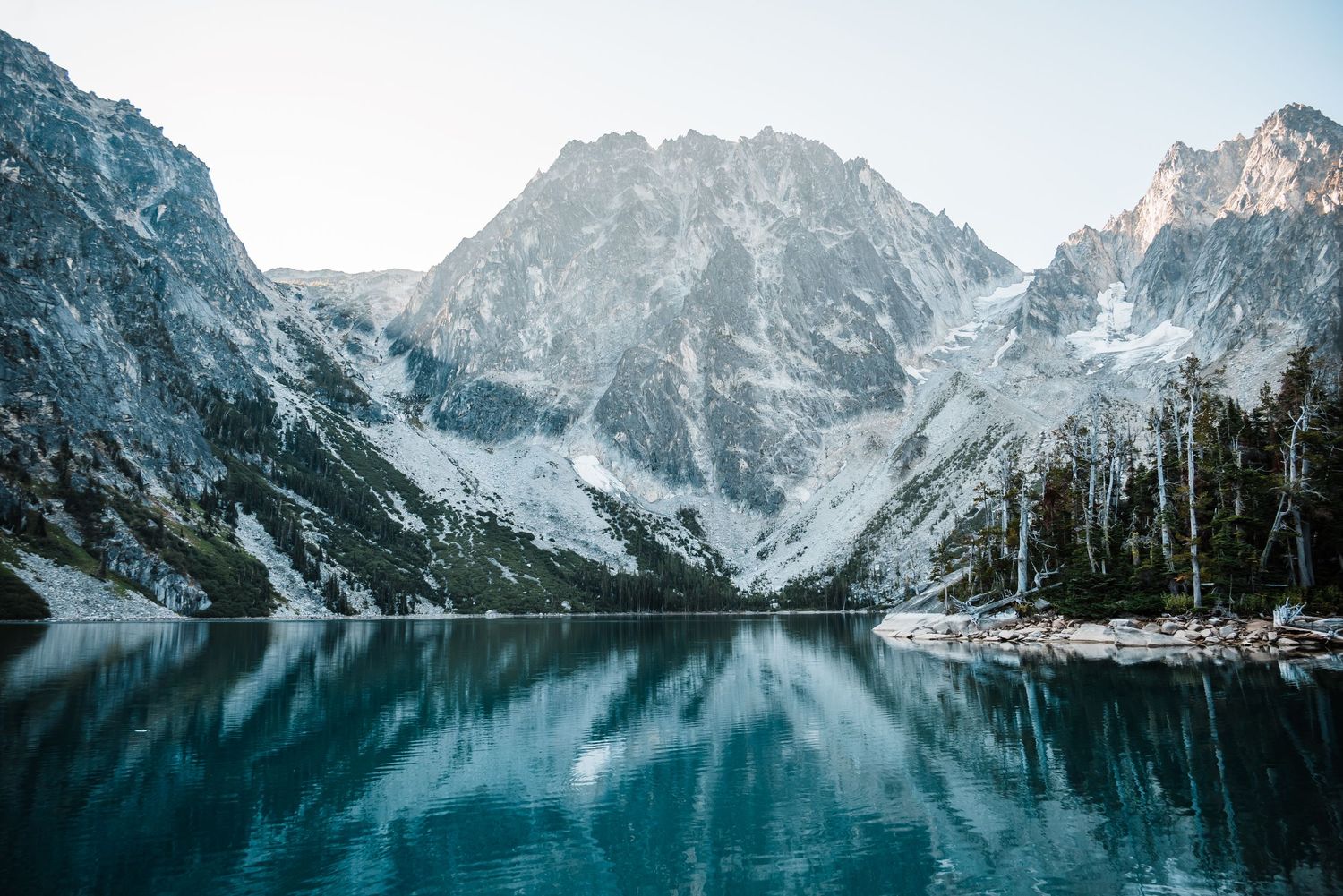 Snowy mountain peaks reflect perfectly in the crystal clear blue waters of a pristine alpine lake.