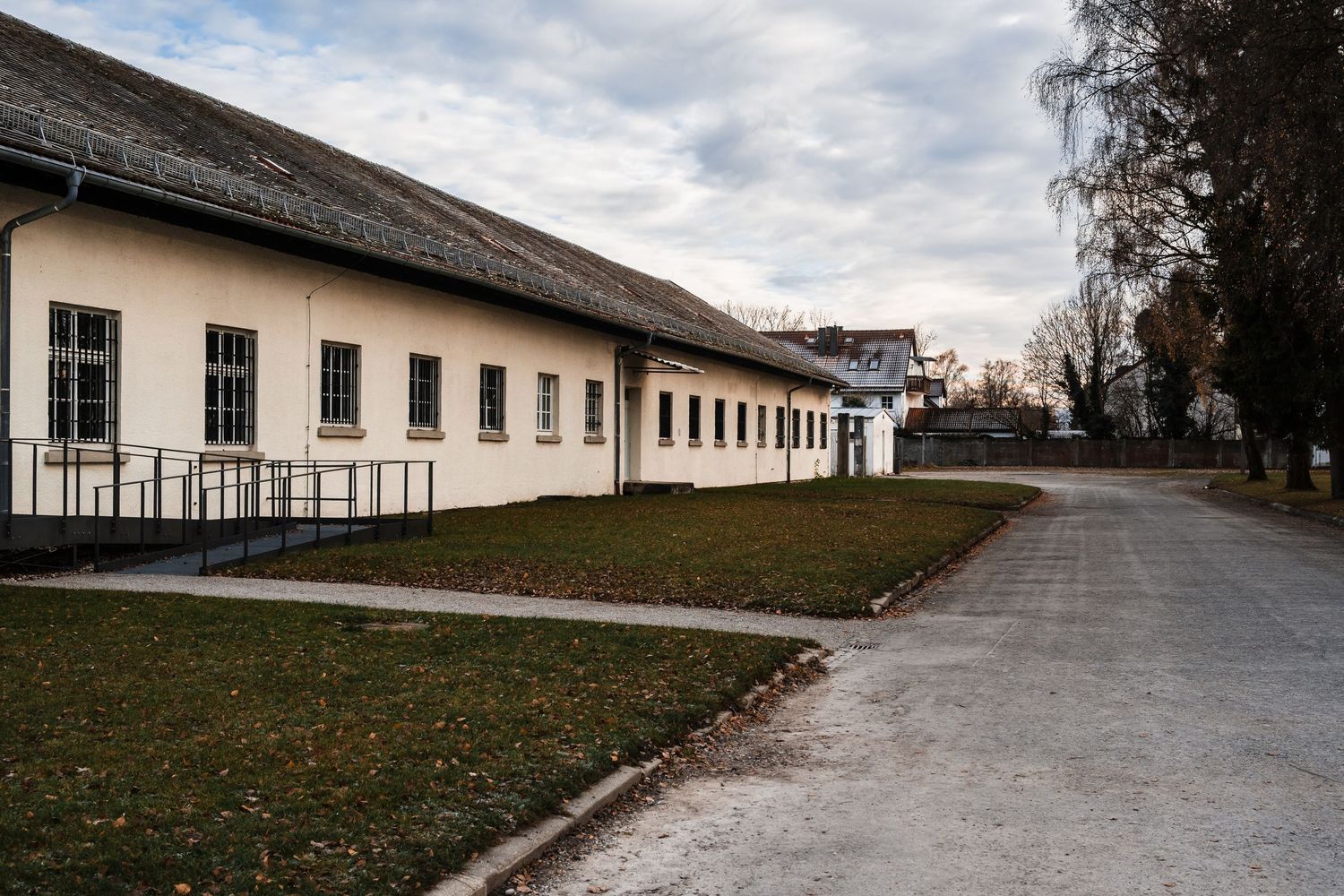 Historic white barracks buildings line a gravel path at a former concentration camp memorial site in Europe.
