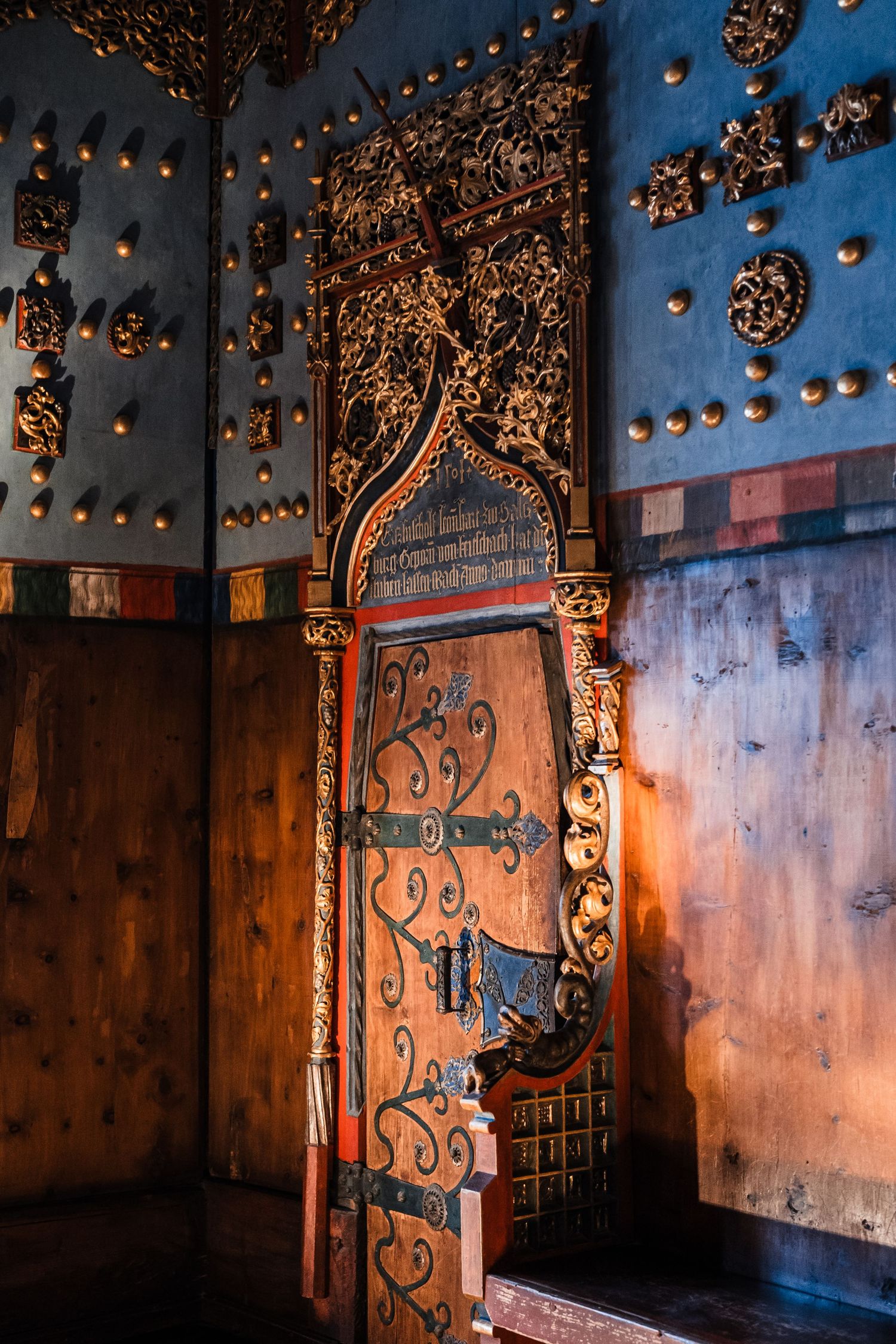 Ornate metal door with decorative scrollwork illuminated by warm lighting against blue walls.