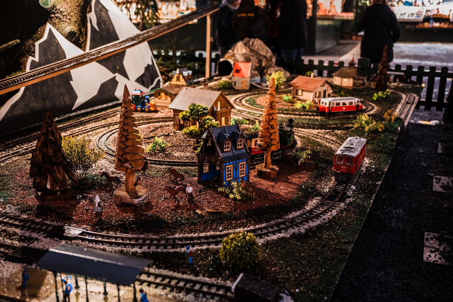 Model train display with miniature village scenes and tracks illuminated with warm lighting at night.