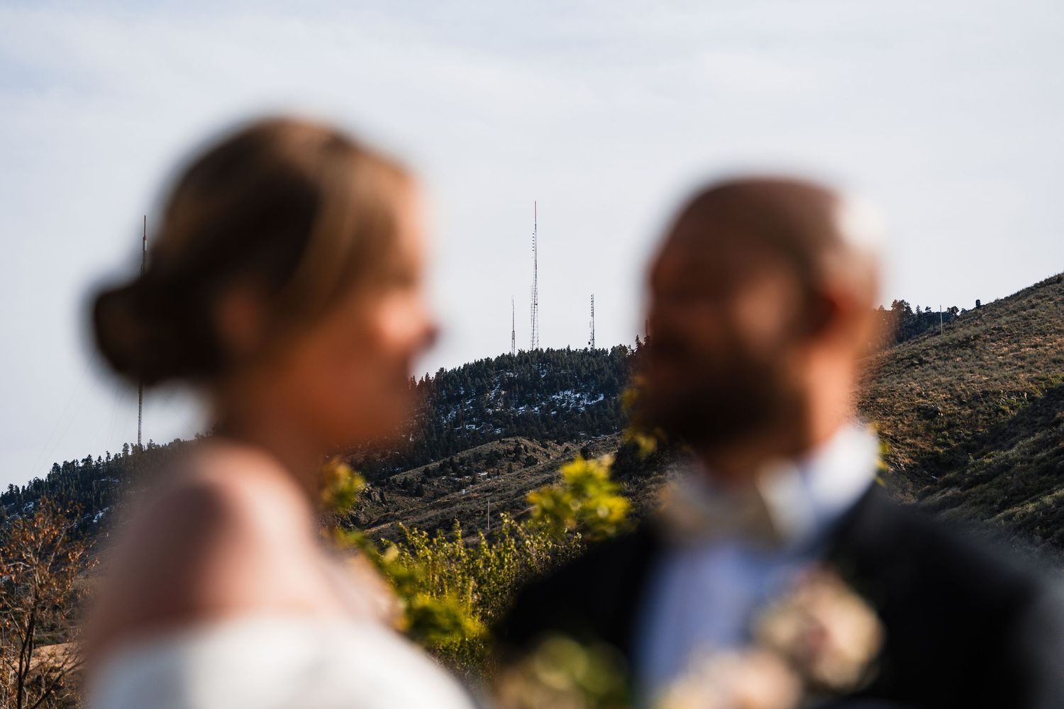 Bride and groom stand blurred in foreground with scenic mountain backdrop at wedding.