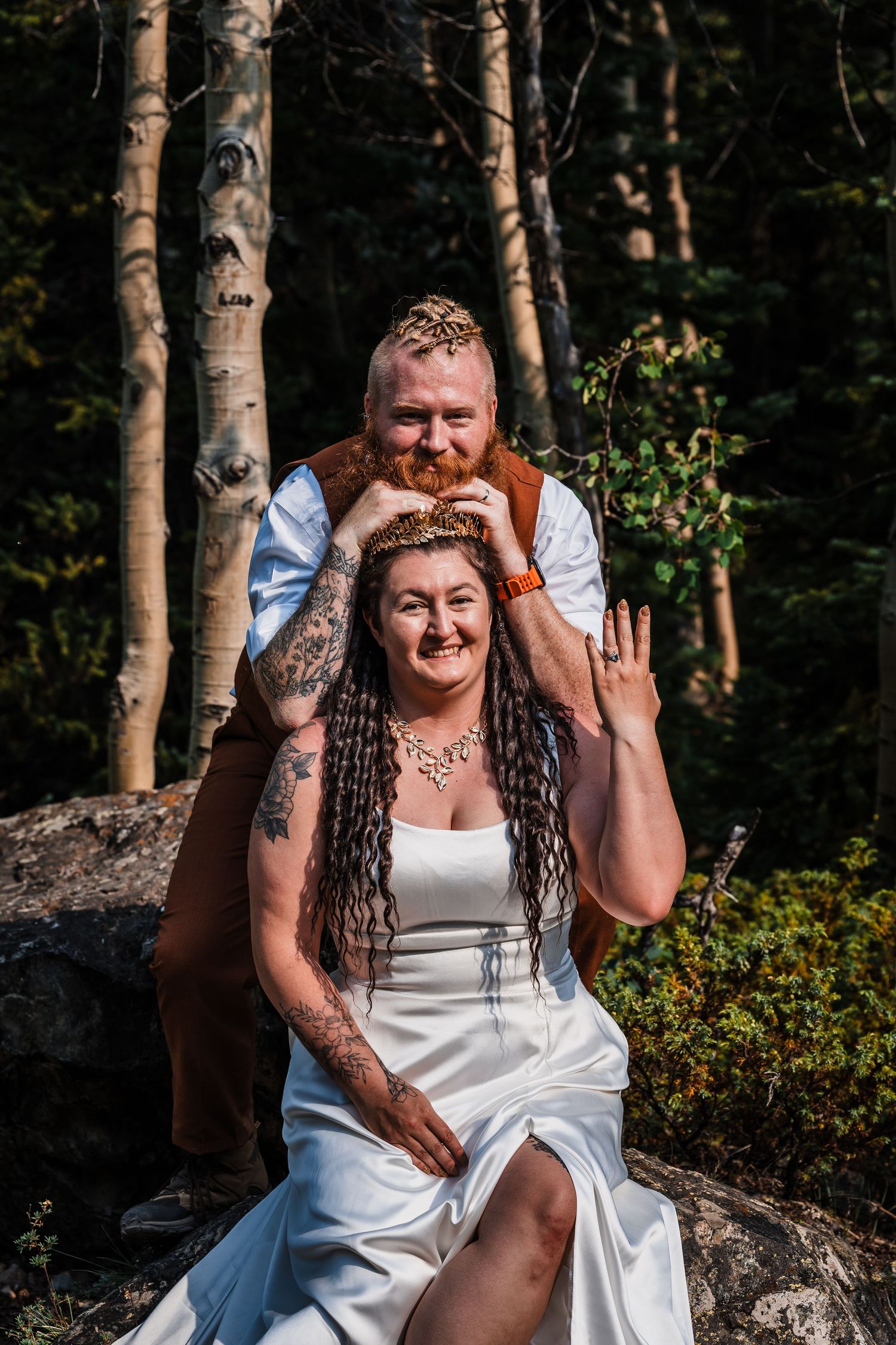 Tattooed couple poses in forest during boho mountain elopement, bride showing wedding ring.