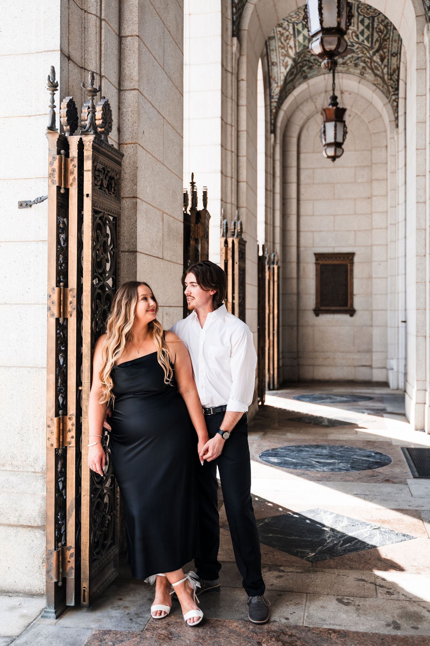 A couple sits together in an elegant arched hallway with stone columns and ornate lanterns.