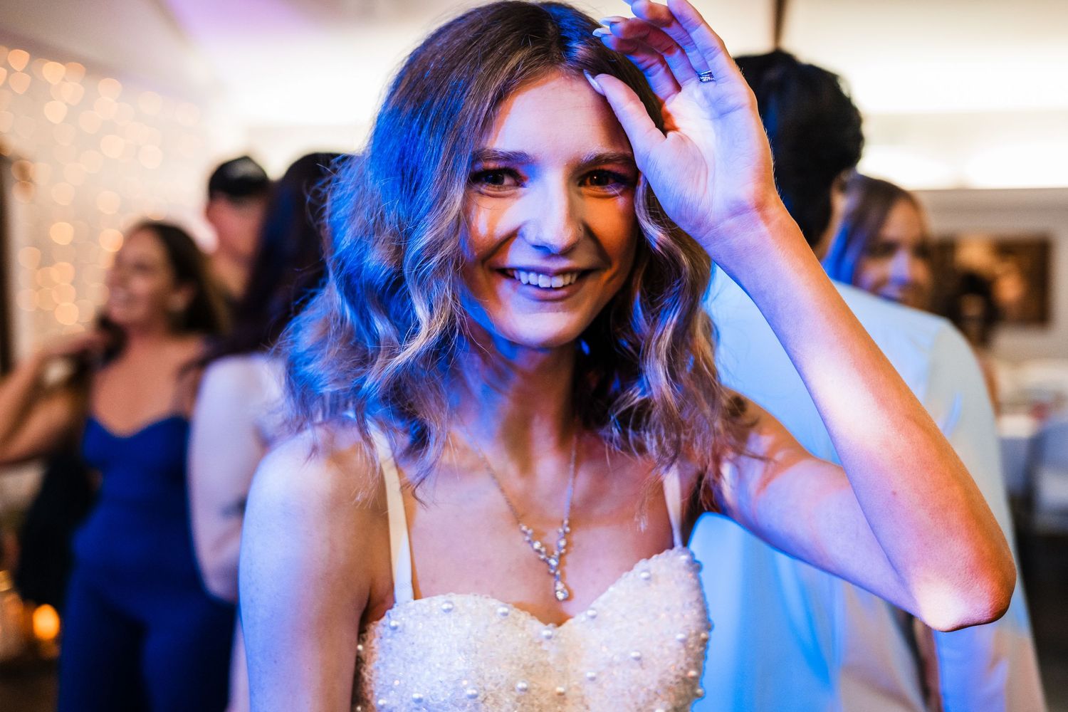 A person in a white bridal dress smiles joyfully during an evening celebration with blue lighting.