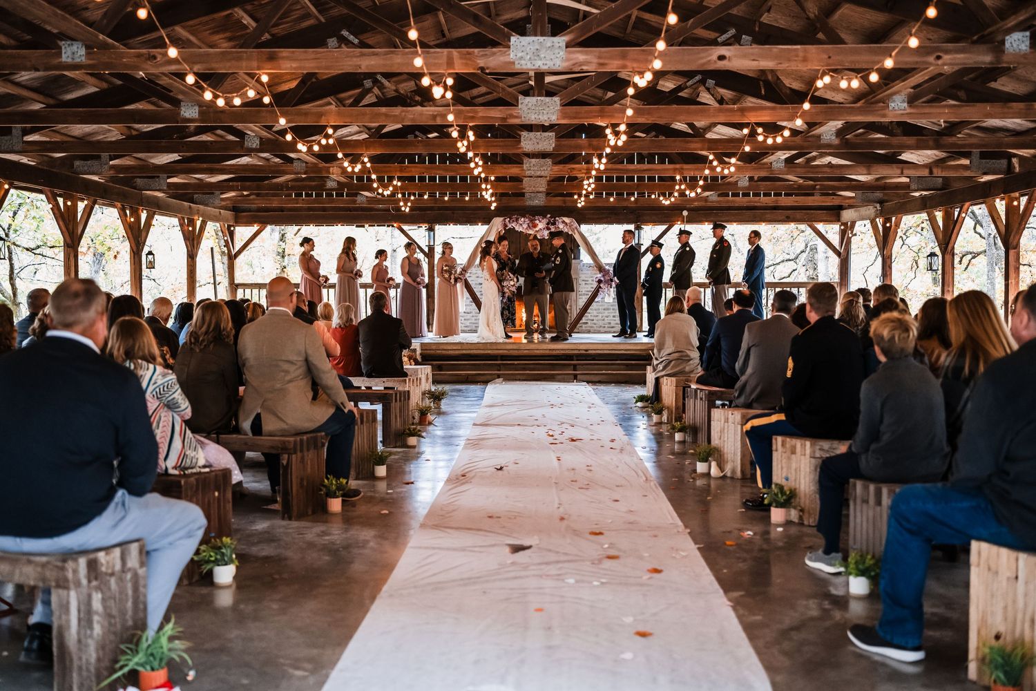 A rustic barn wedding venue with exposed wooden beams and string lights creating a warm, romantic atmosphere.