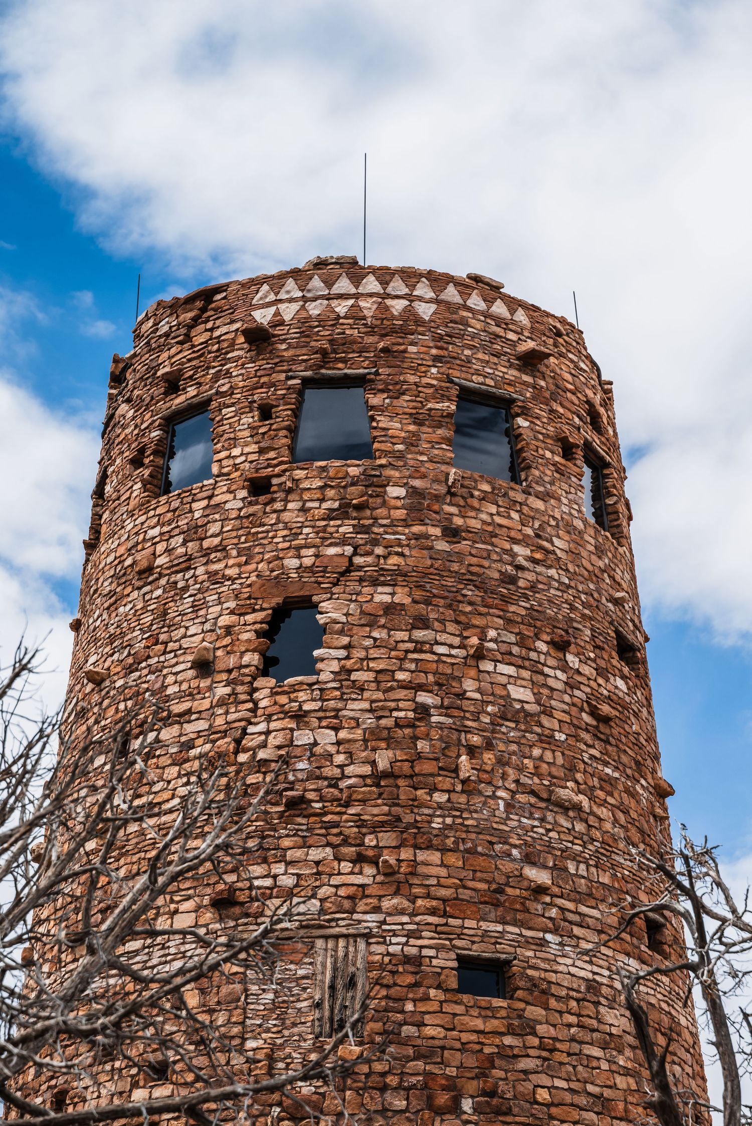 Ancient stone watchtower with circular architecture stands against blue sky with white clouds.