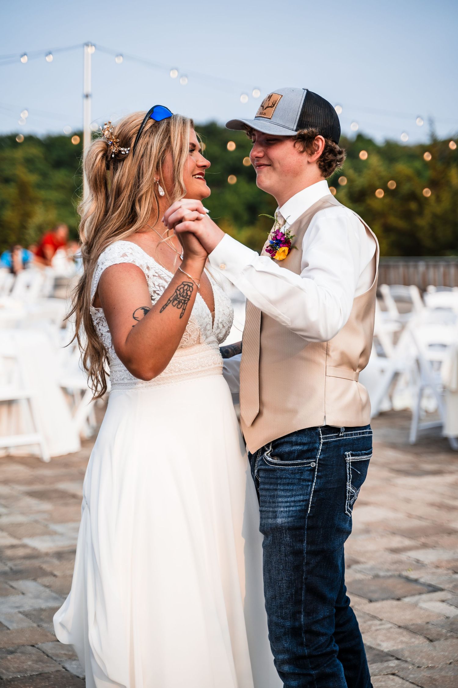 Newlyweds embrace while dancing during a rustic outdoor wedding reception with twinkling lights.