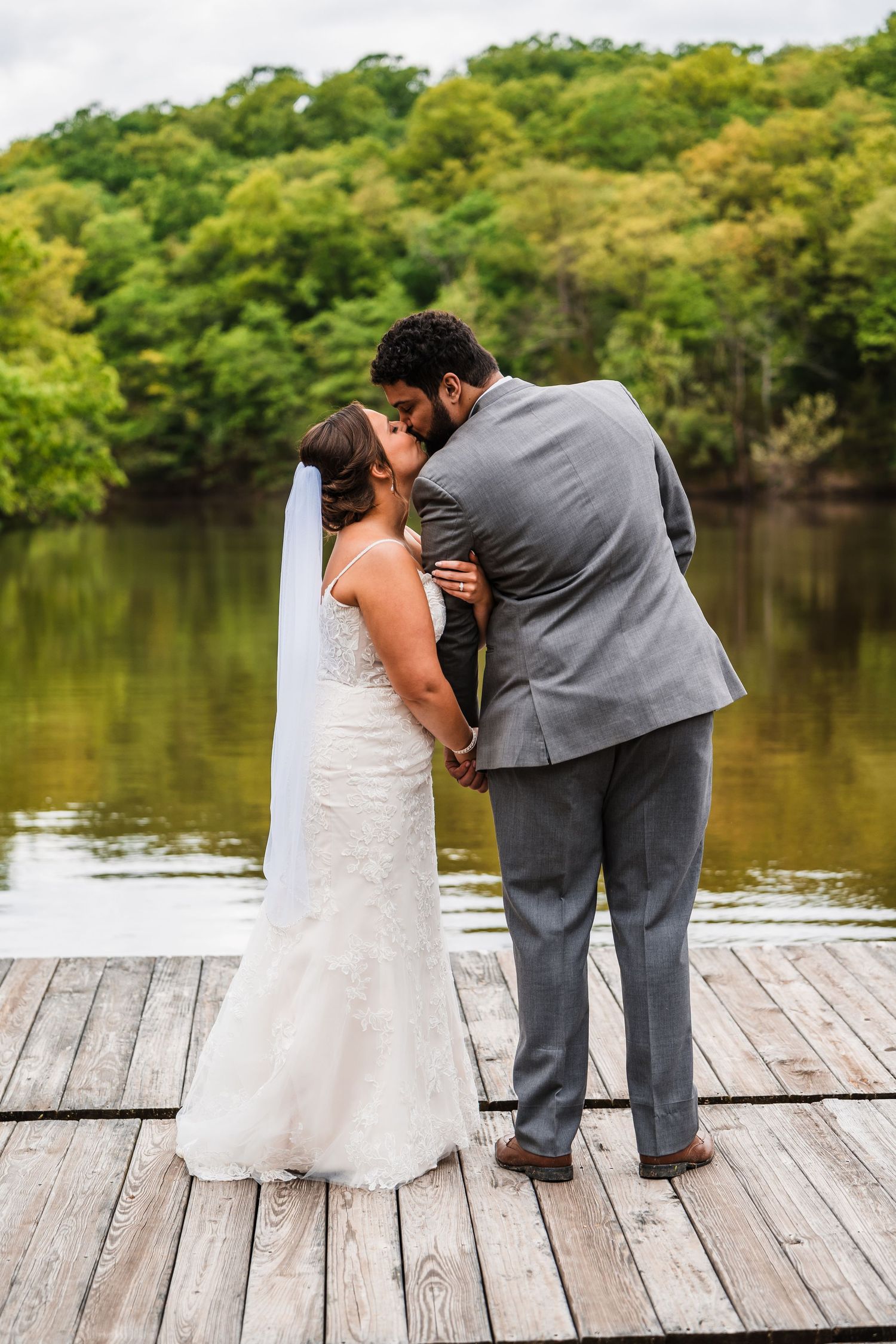 A couple shares an intimate moment on a wooden dock overlooking a serene lake during their wedding.
