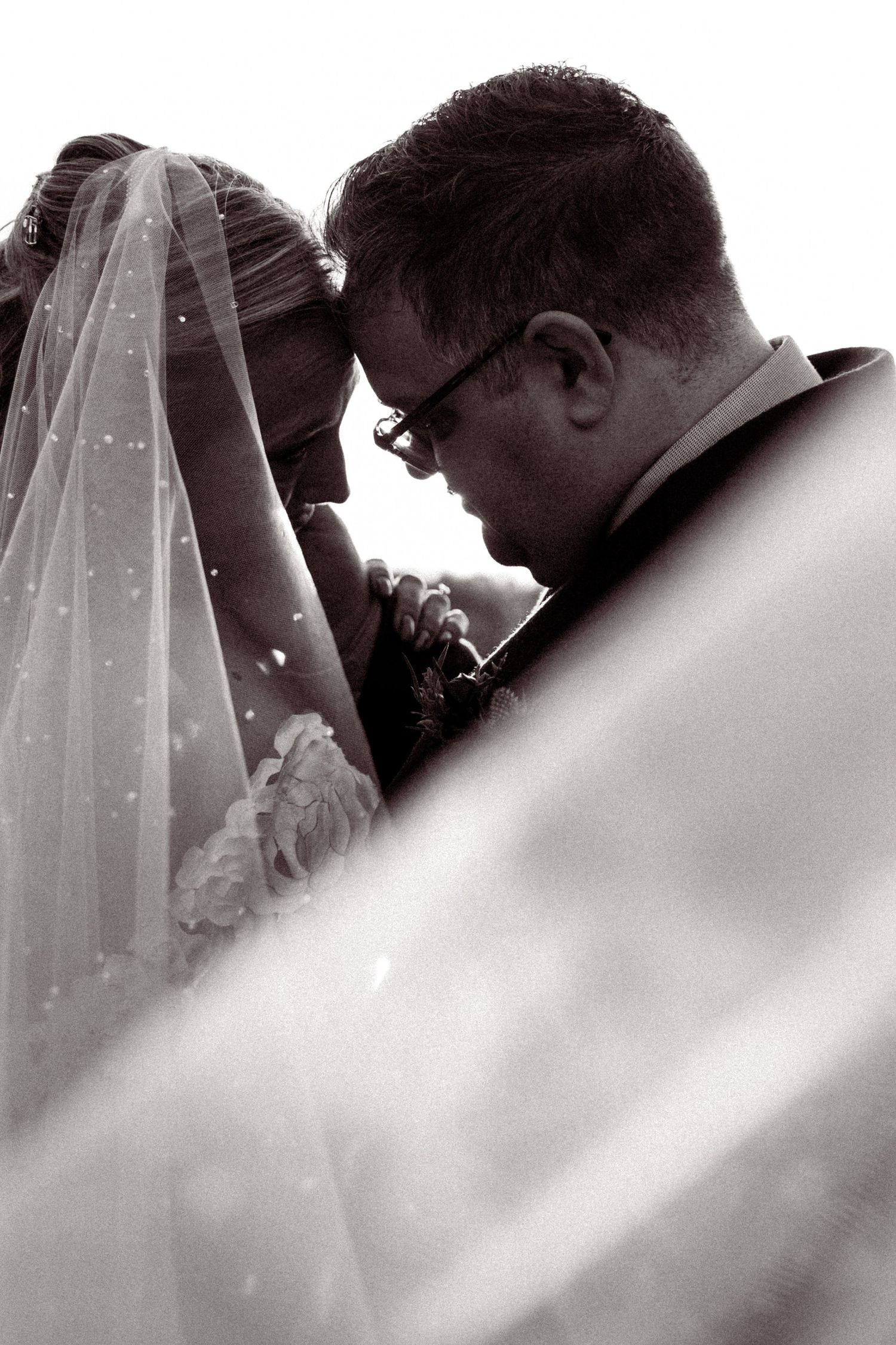 Black and white artistic wedding photo showing intimate moment through delicate veil details.