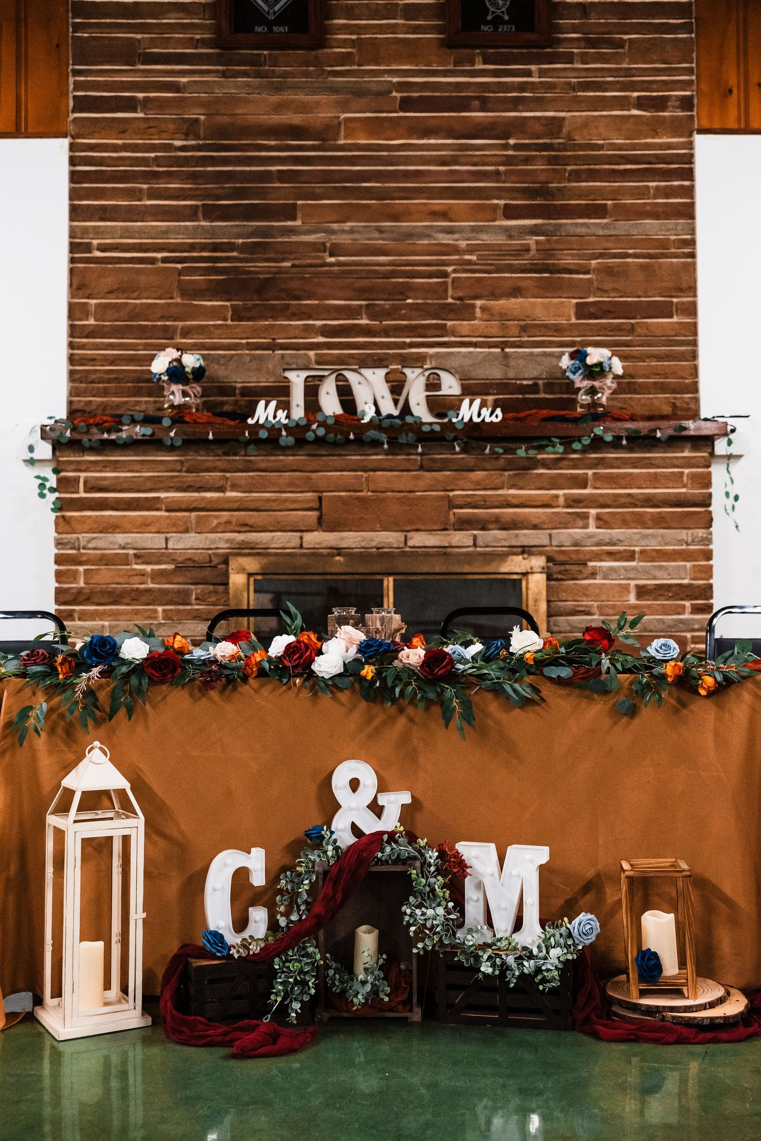 Rustic wooden wall decorated with white letters, lanterns, and floral garlands for a wedding reception.