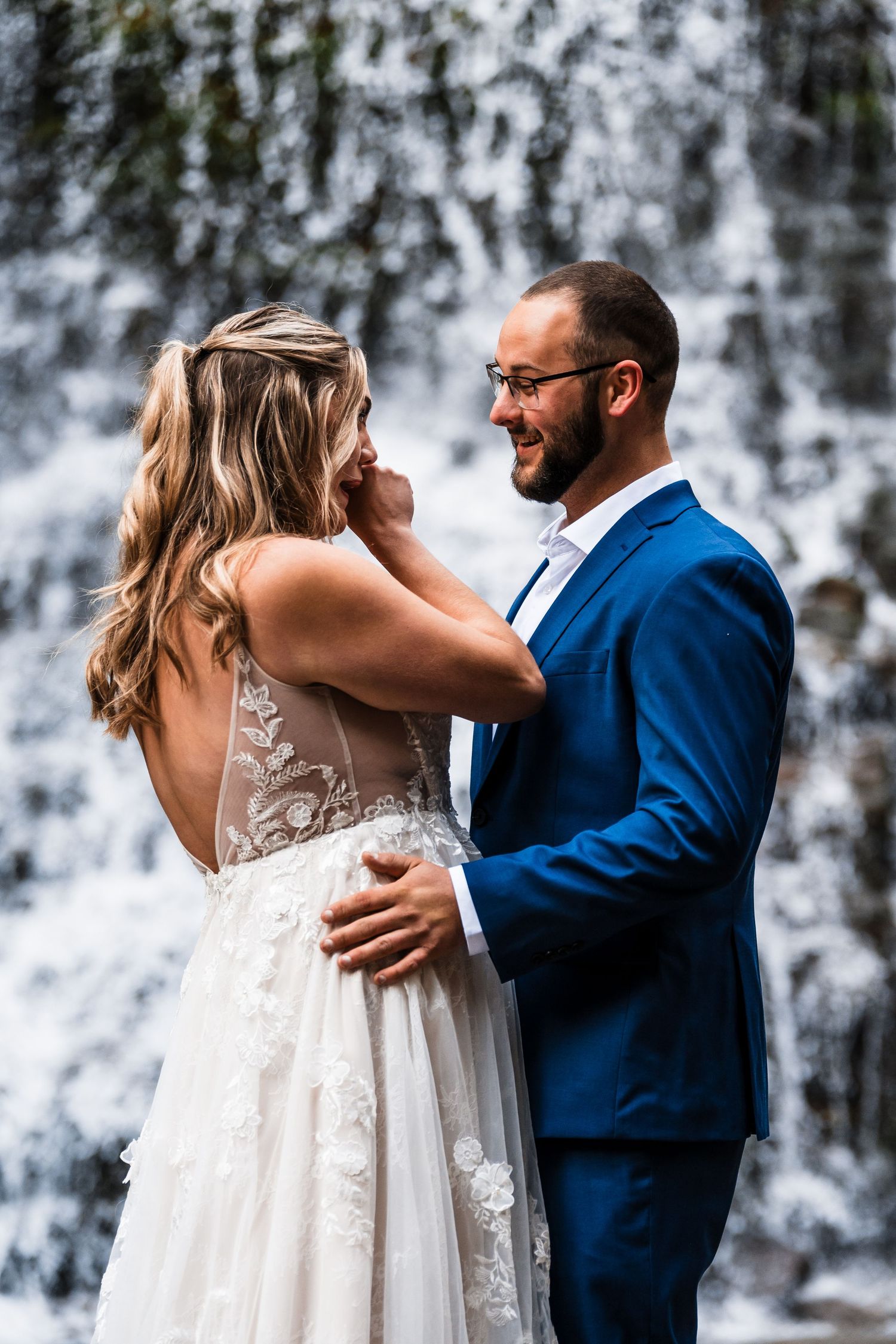 A couple shares an intimate moment in front of a cascading waterfall backdrop.