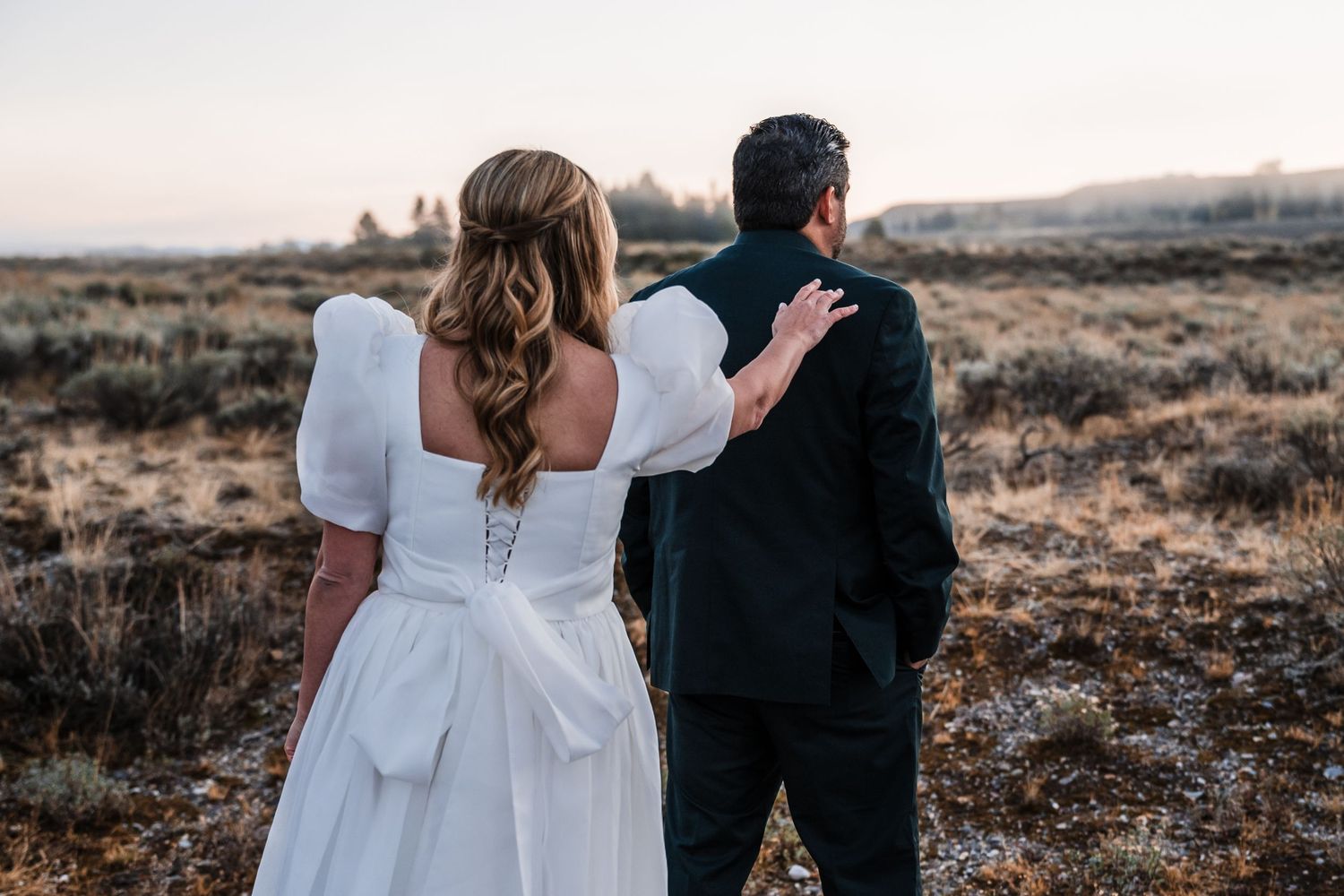 Wedding couple walks hand in hand through desert landscape during romantic sunset photography session.