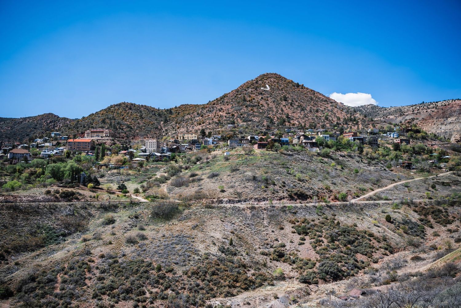 Houses dot the rocky hillside of a desert mountain landscape under bright blue skies in Jerome, Arizona.