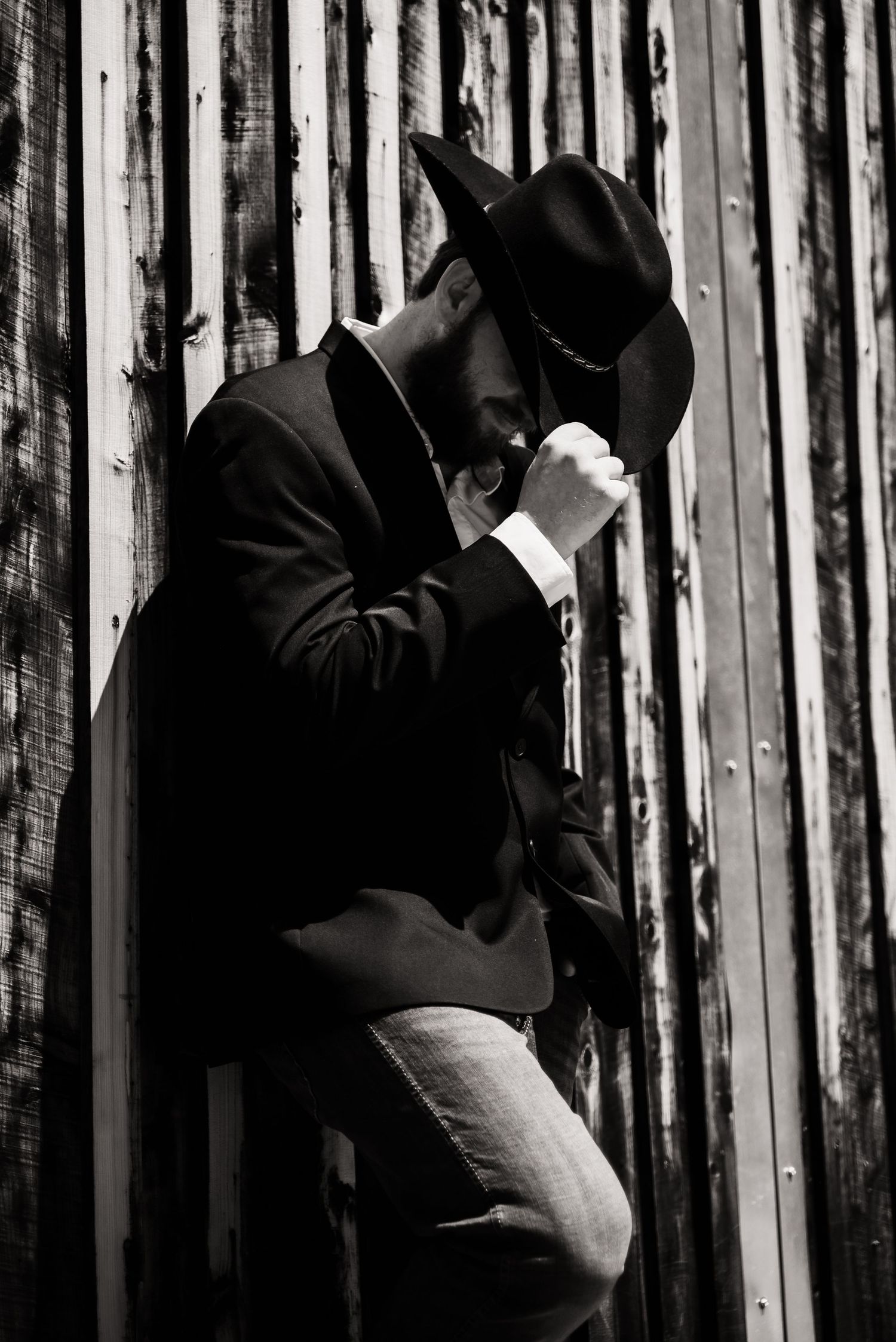 Black and white photo of someone in a cowboy hat and suit leaning against a striped wall.