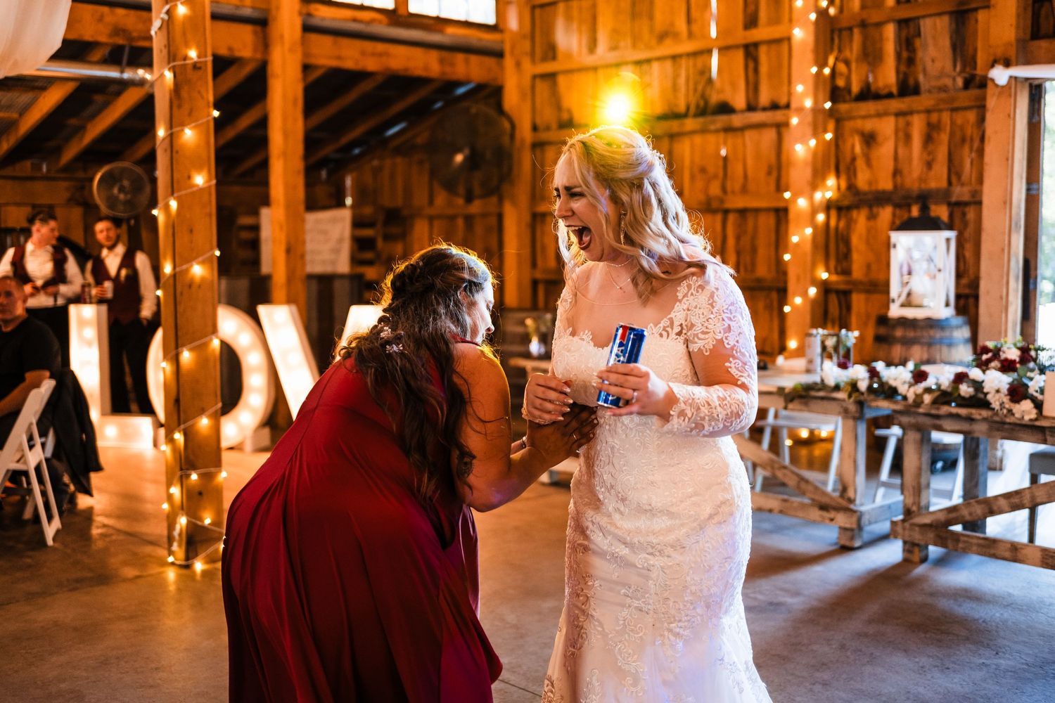Intimate moment during wedding reception in rustic barn venue with warm lighting.