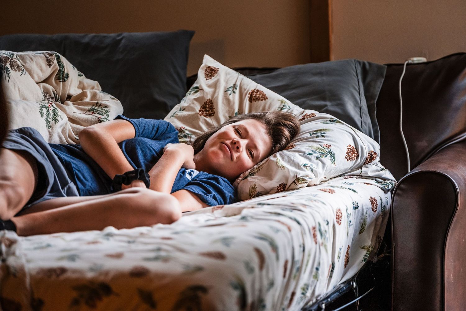 A person naps peacefully on a floral patterned couch in natural lighting.