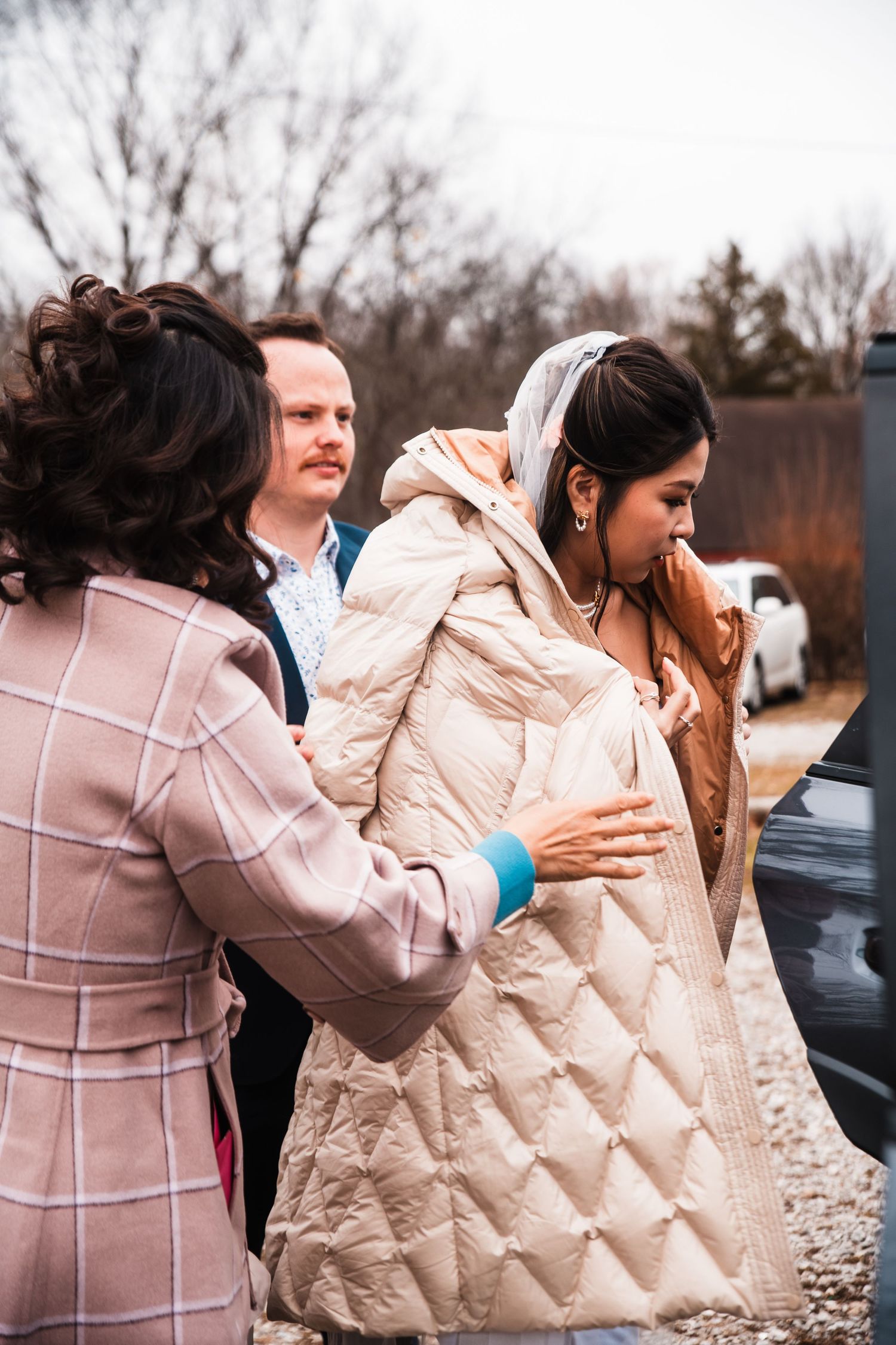 People help the bride with a quilted coat on a chilly autumn day.