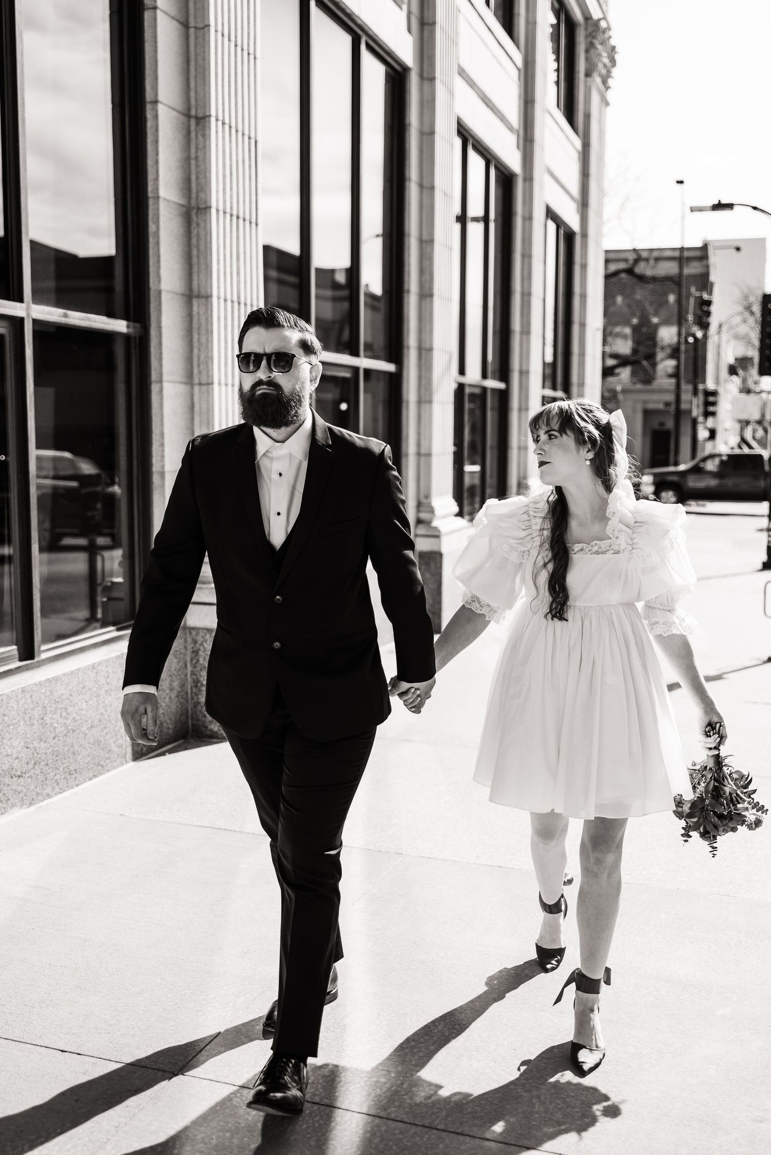 Black and white photo of couple walking down urban sidewalk after wedding ceremony.