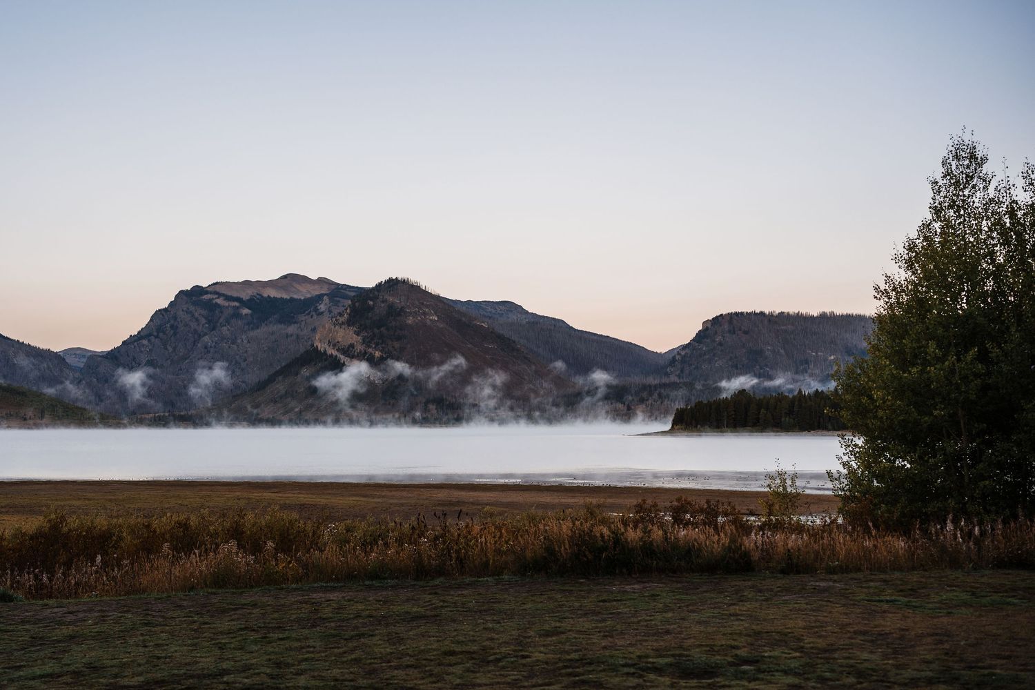 Scenic mountain landscape with fog rolling over hills and trees during a misty morning at sunrise.