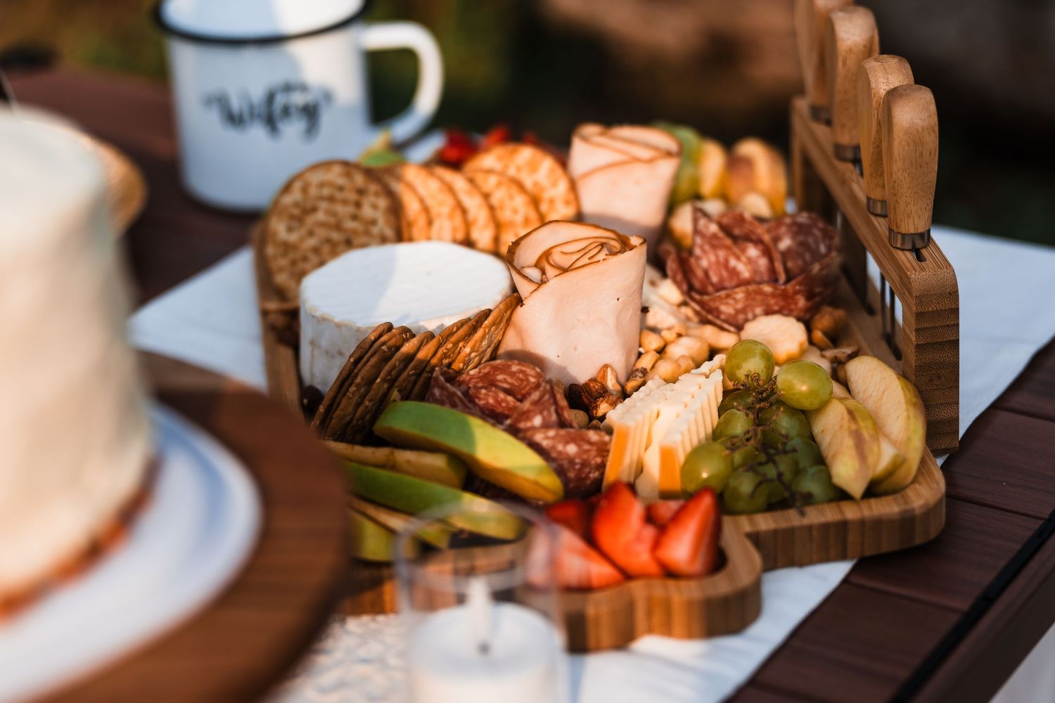 Rustic wooden charcuterie board with cheese, meats, fruits and crackers at outdoor wedding reception.