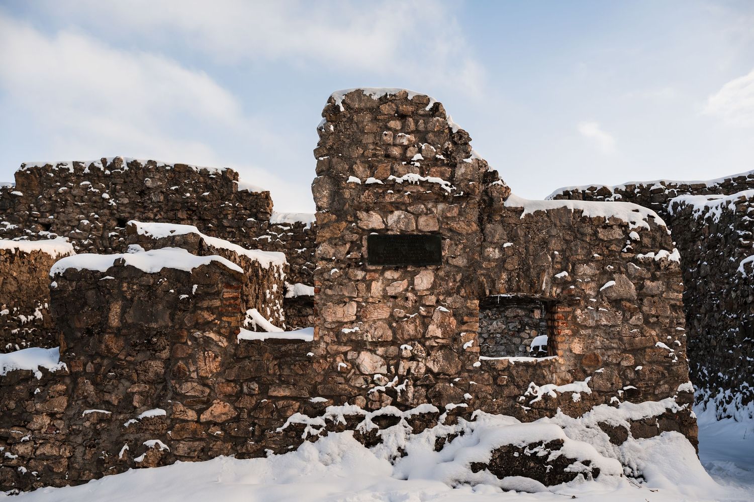 Ancient stone ruins covered in snow stand against a mountainous winter landscape.