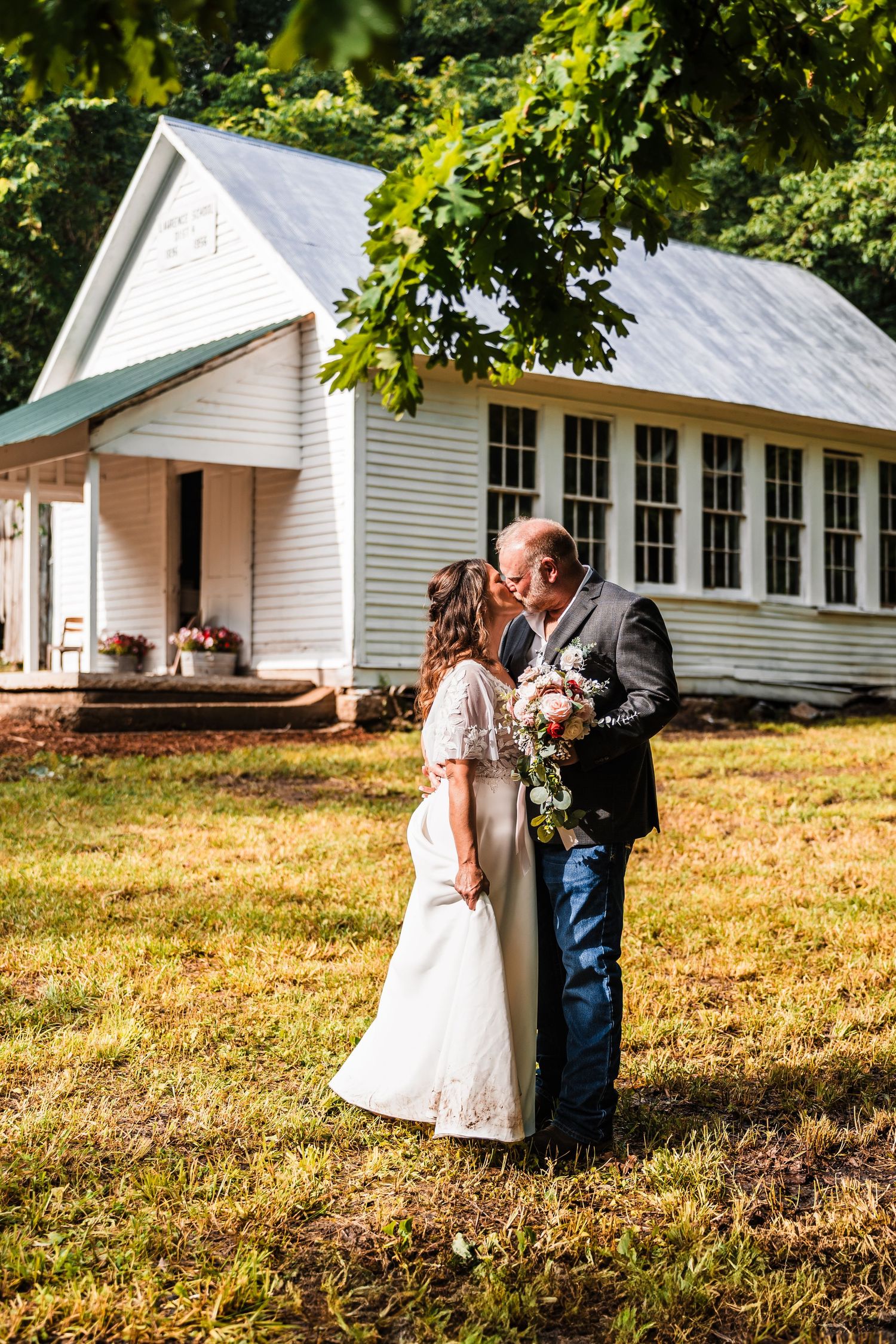 Wedding couple poses outside a traditional white clapboard church building on a sunny day.