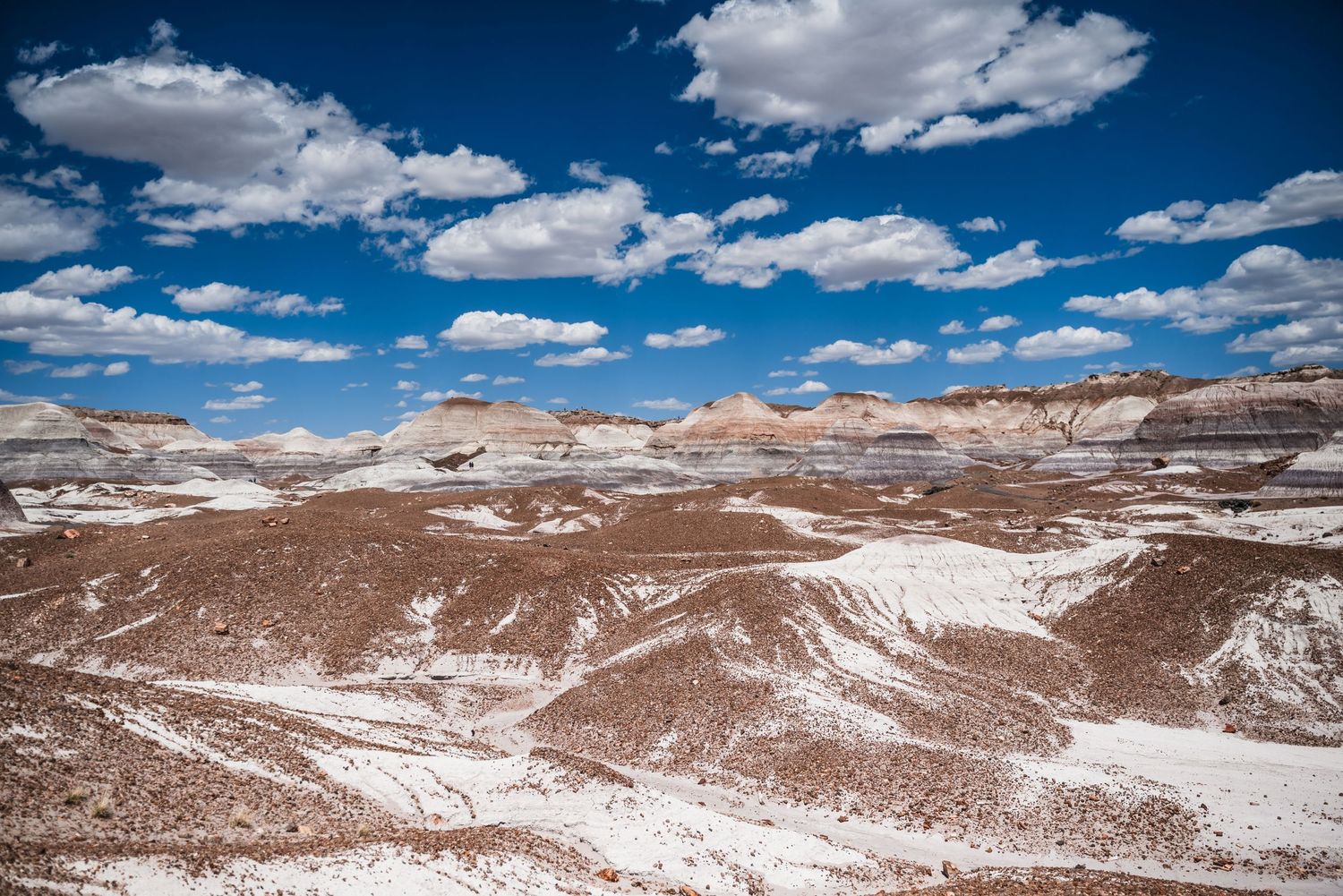 Dramatic desert landscape with white striped hills under bright blue sky with puffy clouds.