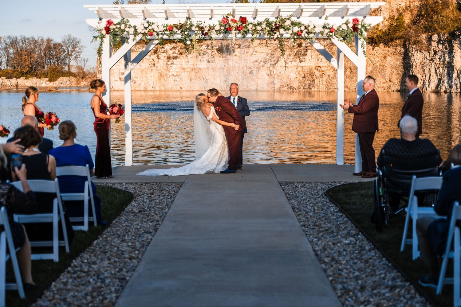 Outdoor wedding ceremony under floral arch with quarry lake and cliff backdrop.