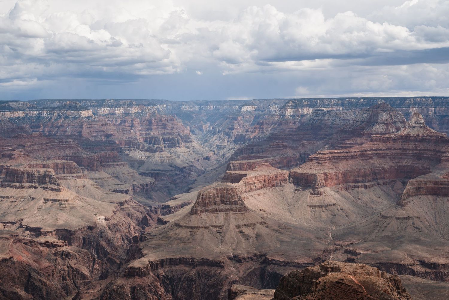 Dramatic aerial view of the Grand Canyon showing layered rock formations under cloudy skies.