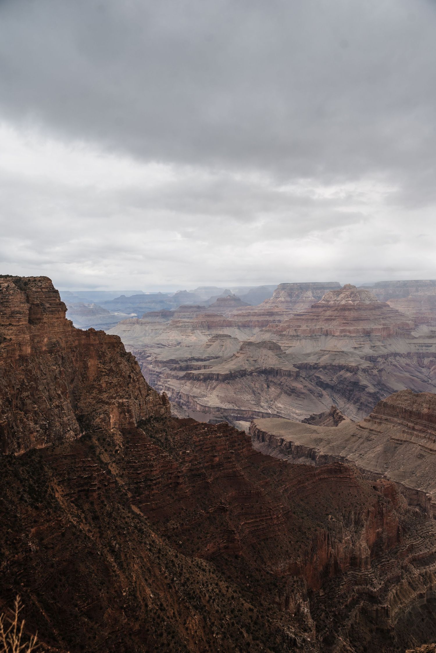 A moody vista of the Grand Canyon's deep gorges and rock layers under an overcast sky.