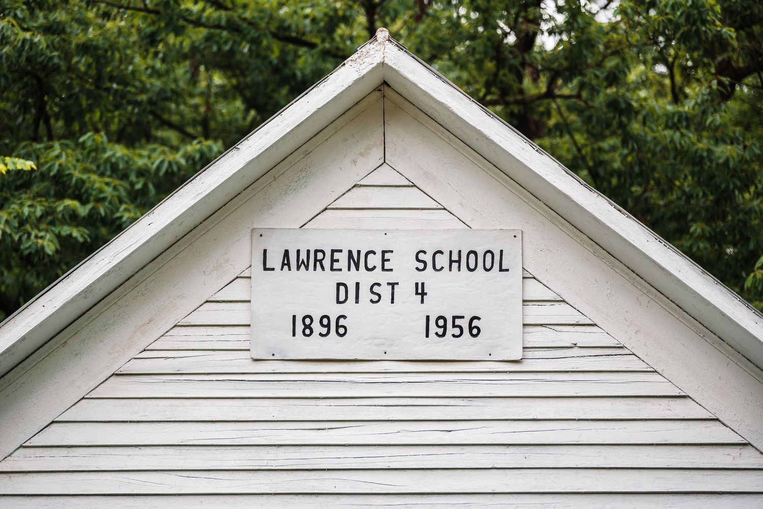 Historical white wood-framed Lawrence School building from 1896 with district details visible on its facade.