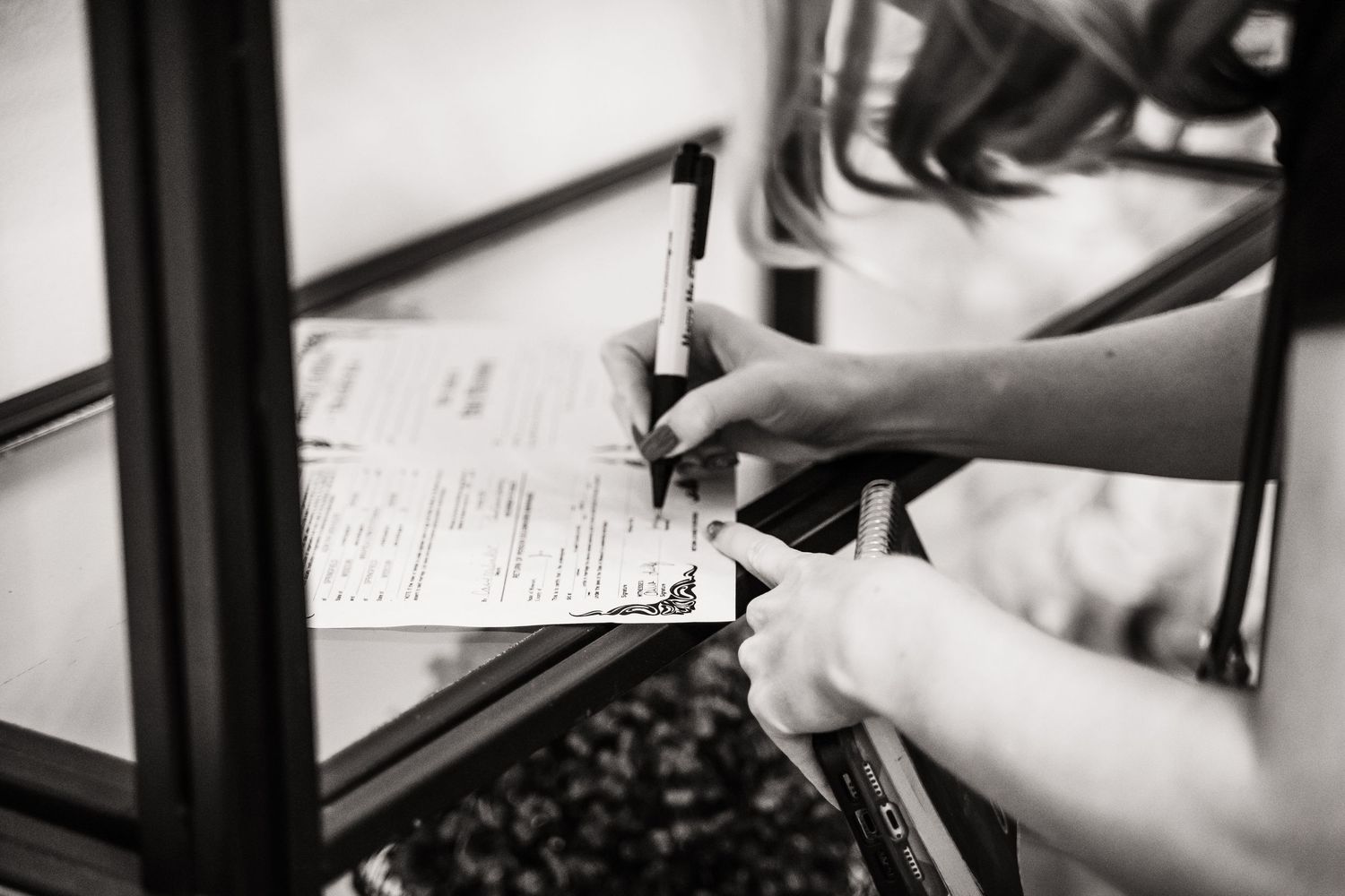 A pair of hands holding a pen while filling out paperwork on a clipboard in black and white.