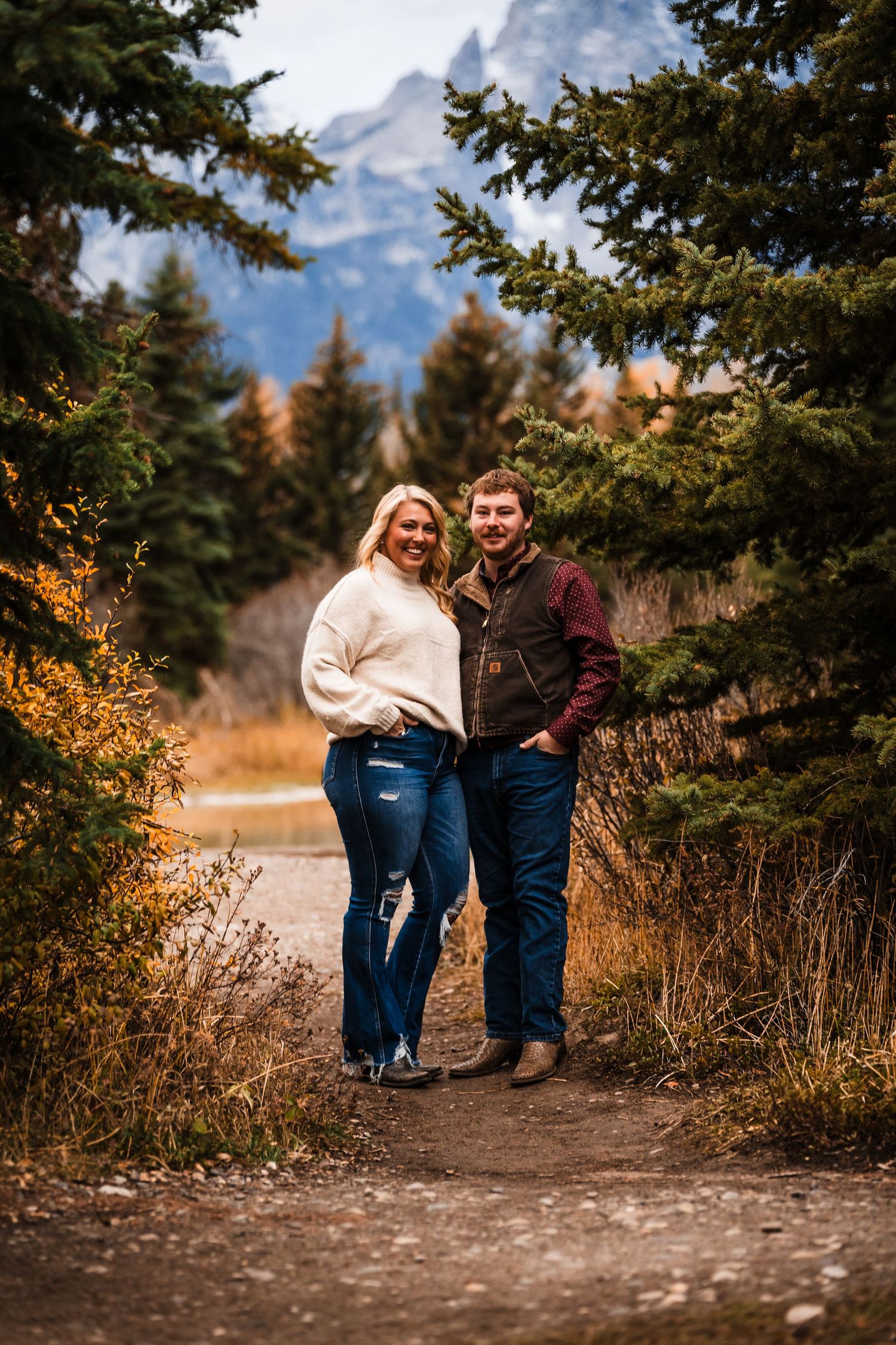 A couple shares a romantic moment on a mountain trail surrounded by autumn foliage and evergreen trees.