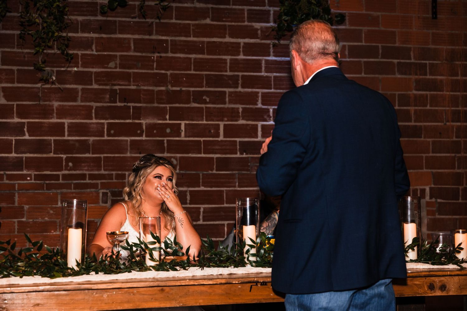 A wedding reception moment at a head table against exposed brick wall with ambient lighting.