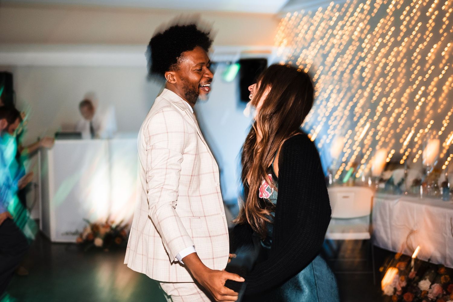 Two people share an energetic dance moment under twinkling string lights.