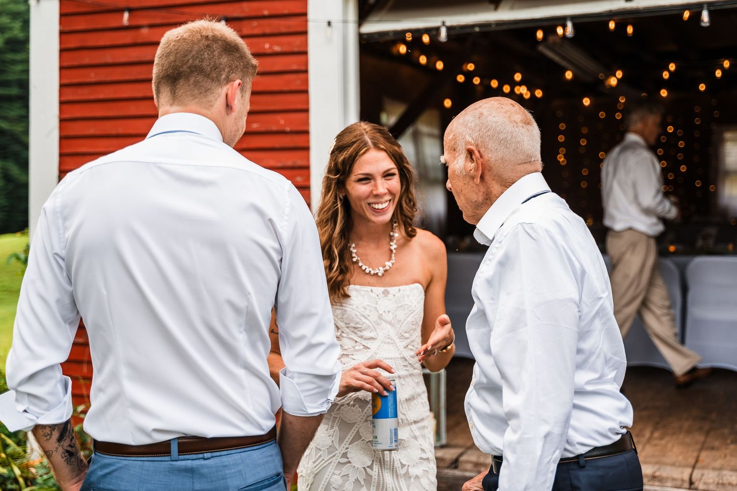 Wedding guests chatting outside a red barn decorated with string lights.