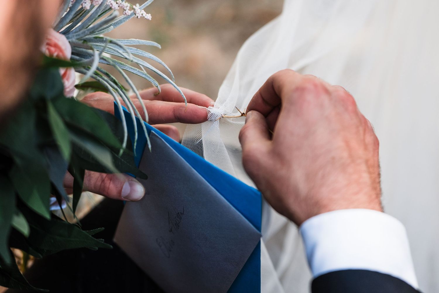 Close-up detail shot of hands pinning a boutonniere with blue accents.