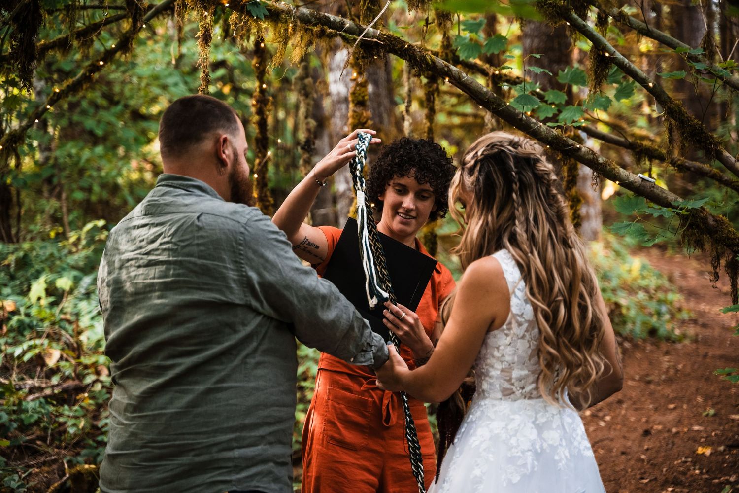 Wedding ceremony in a forest with three people gathered under trees.